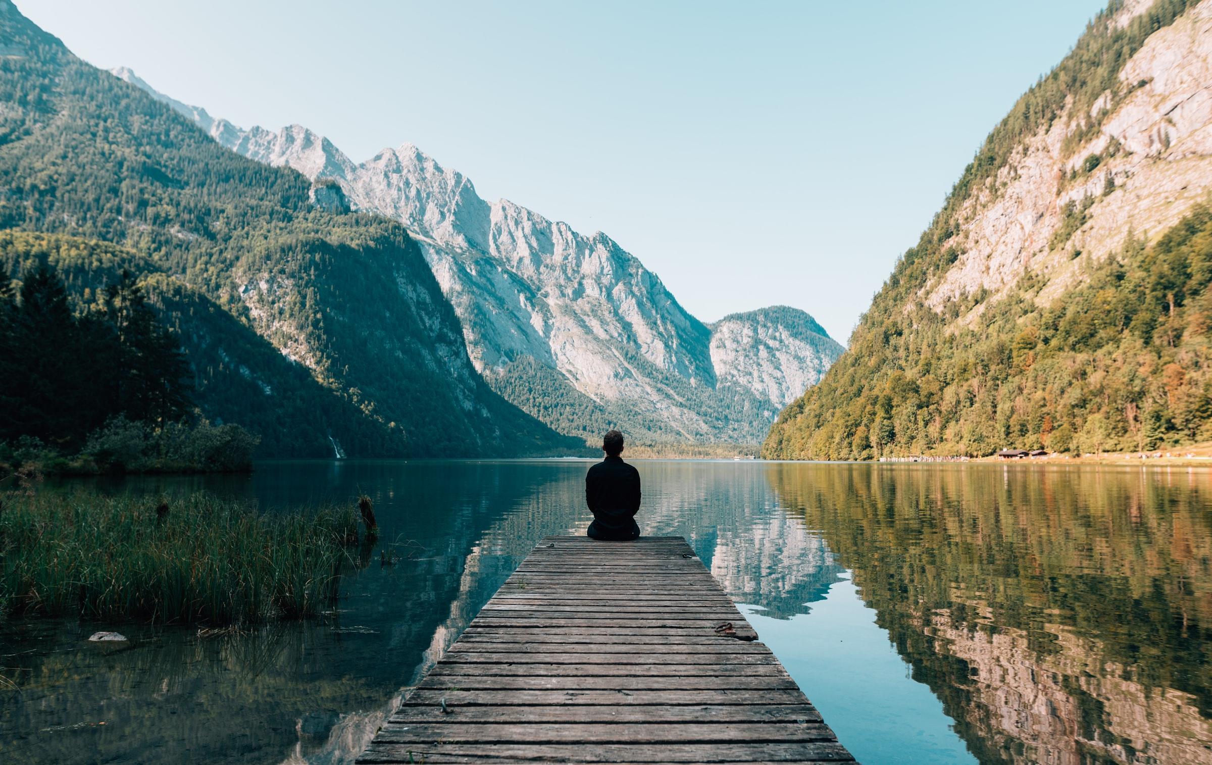 man sitter på bryggar vid sjö i dal som meditation