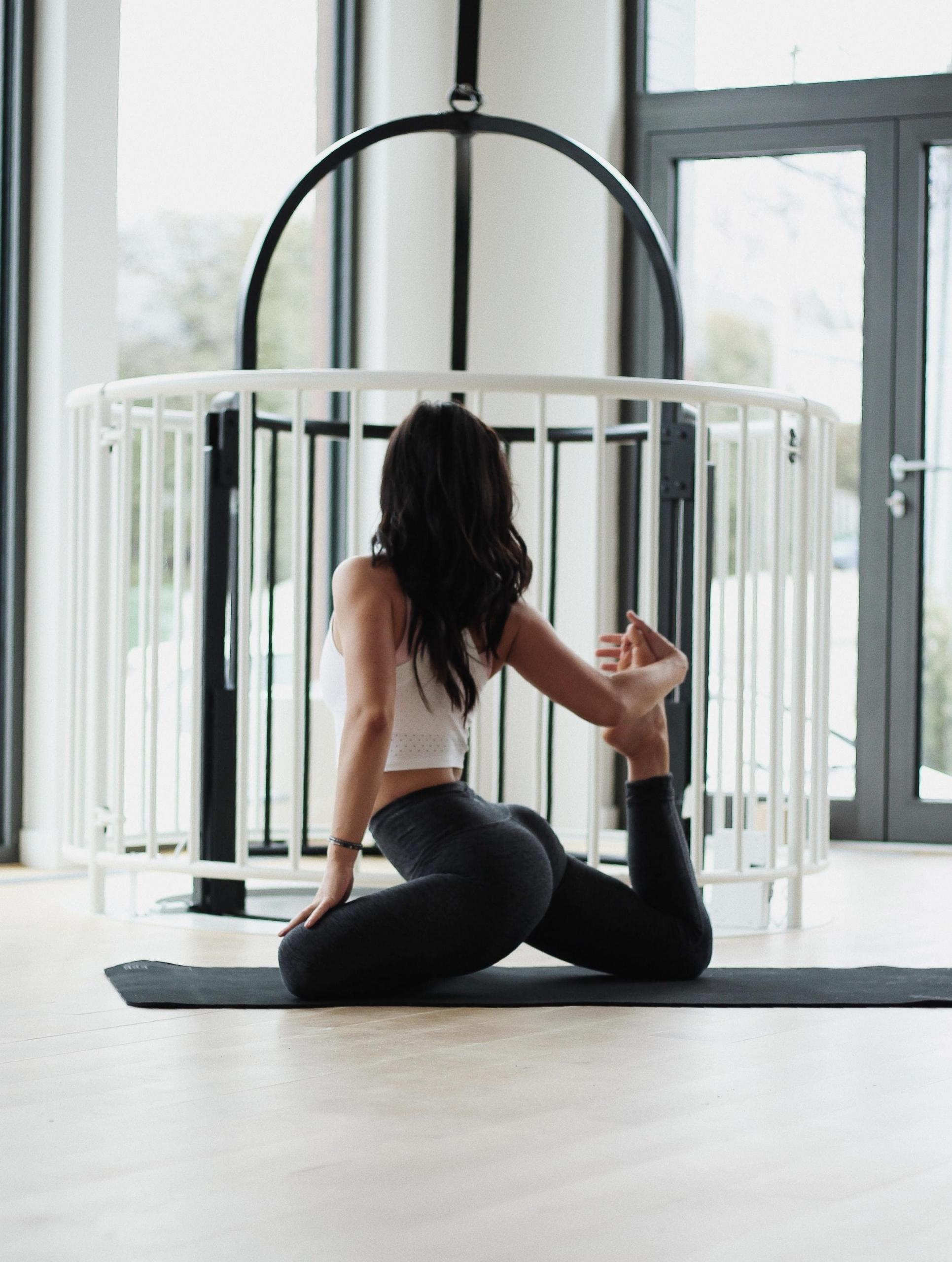 Kvinna med mörkt hår utövar en yogaposition på en svart yogamatta