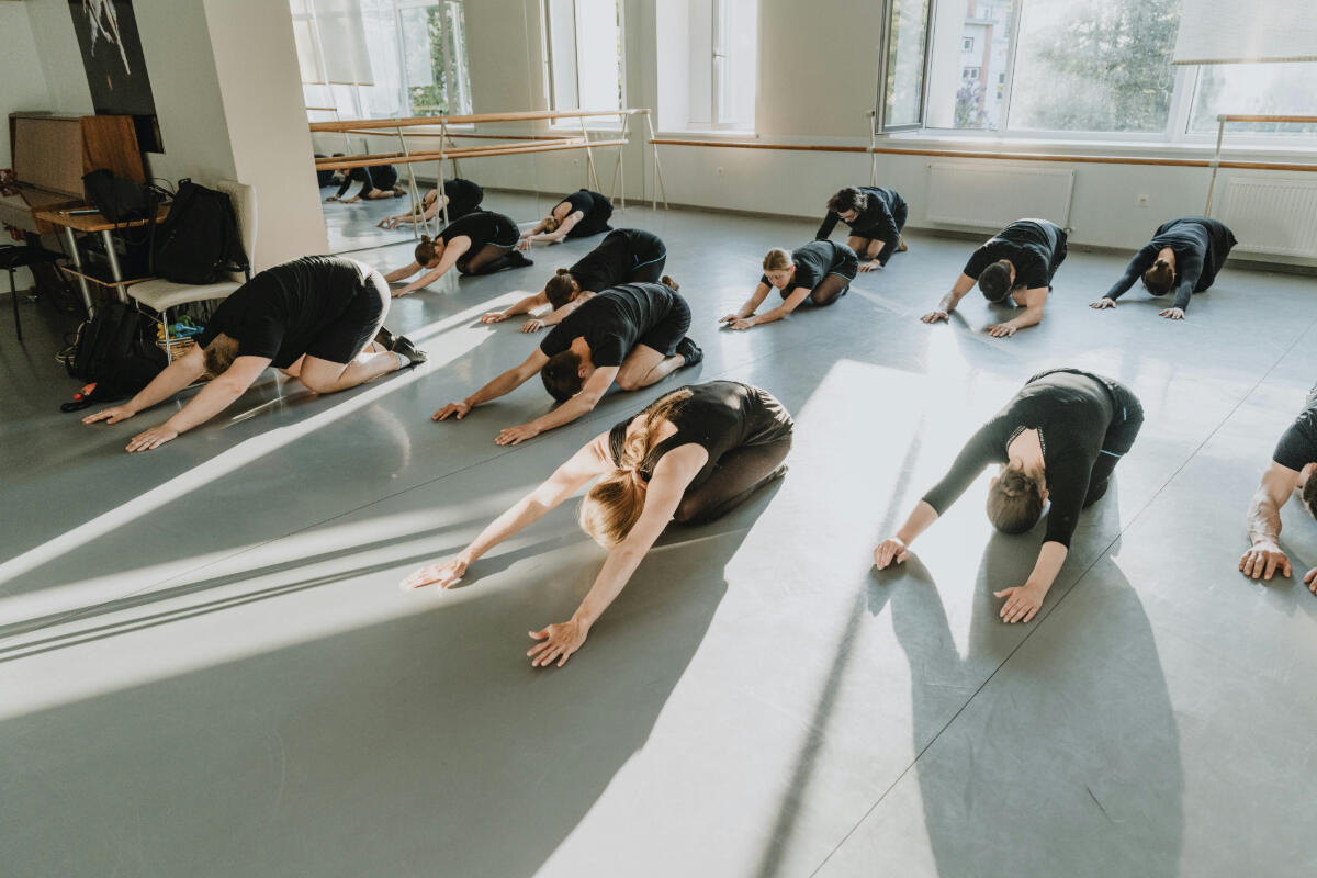 En grupp som utövar yoga tillsammans i ett rum med mycket fönster.