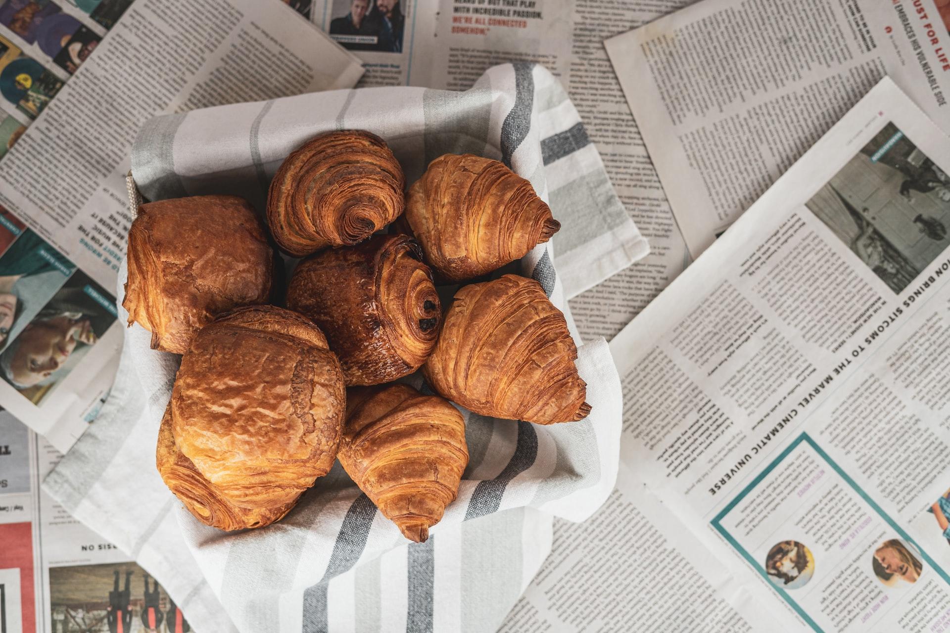 croissanter och pain chocolate i en korg som står på ett bord täckt av franska tidningar