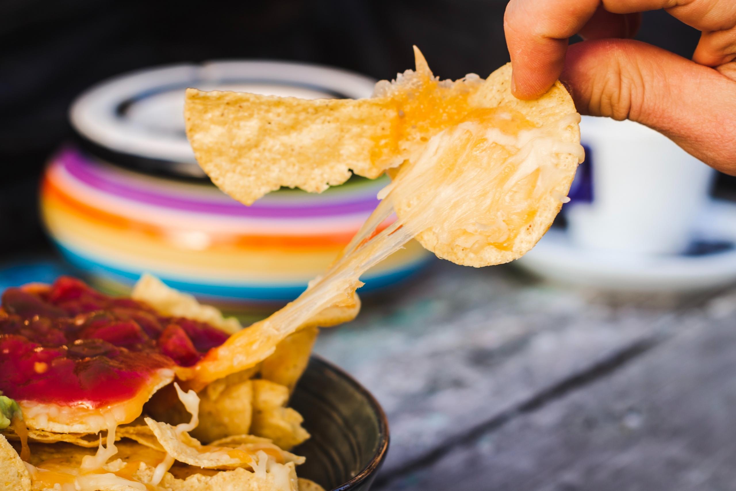 en person tar en nacho med smält ost ur en nachoskål som toppats med salsa