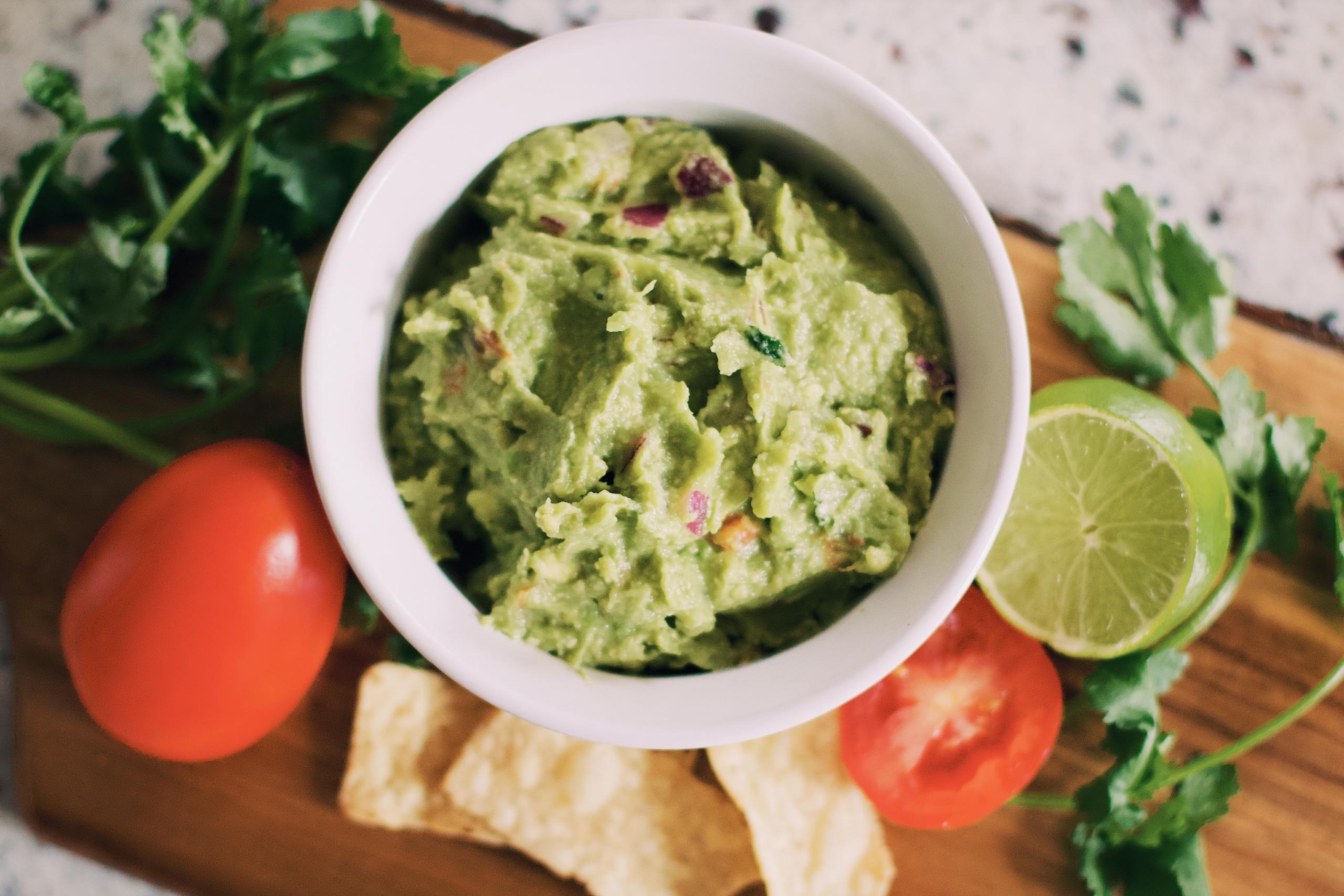 guacamole i skål med lime och tomat vid sidan om