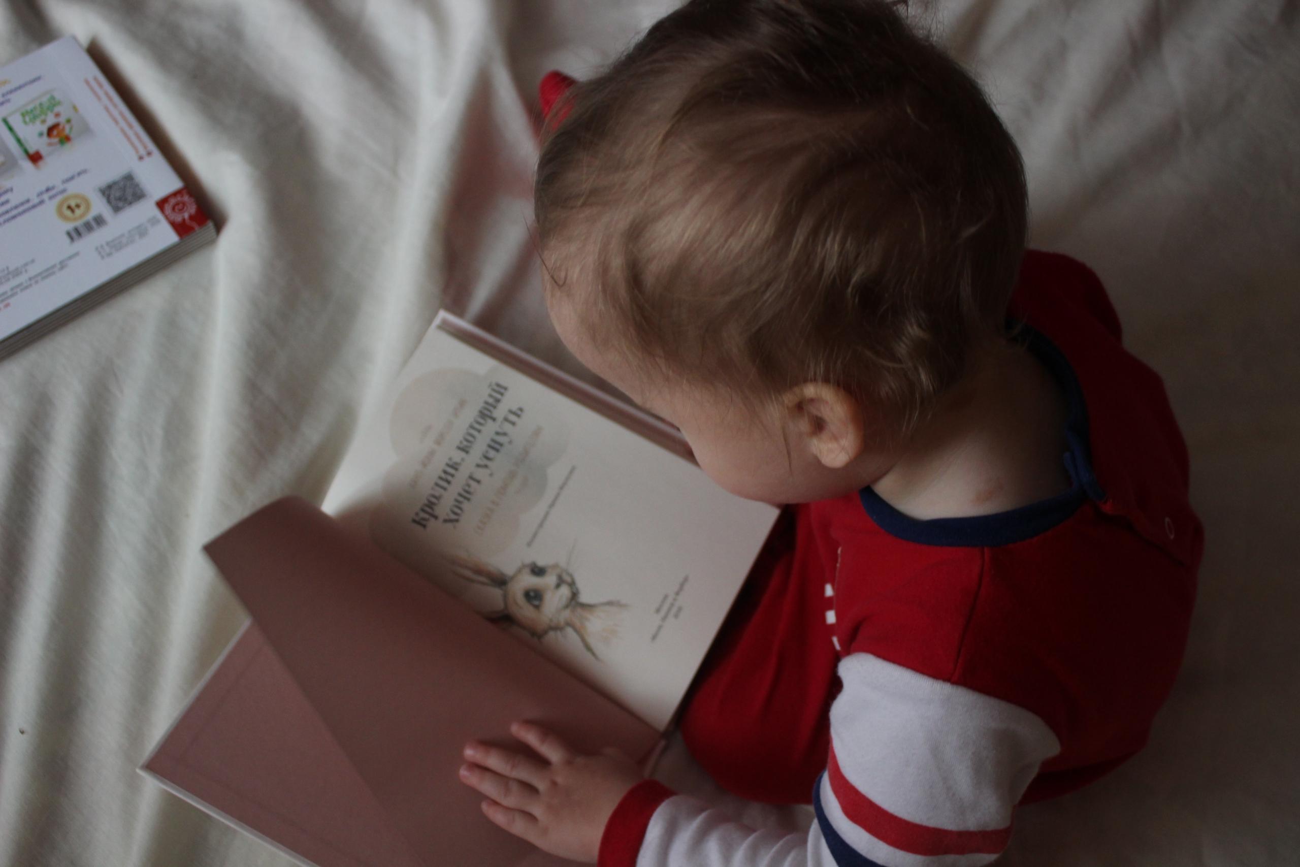 spädbarn sitter i säng med bok i sitt knä