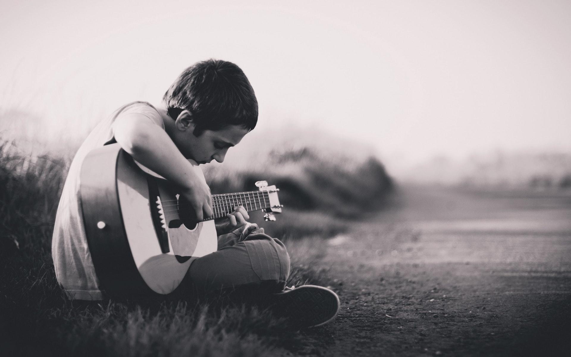 liten pojke spelar gitarr vid vägen