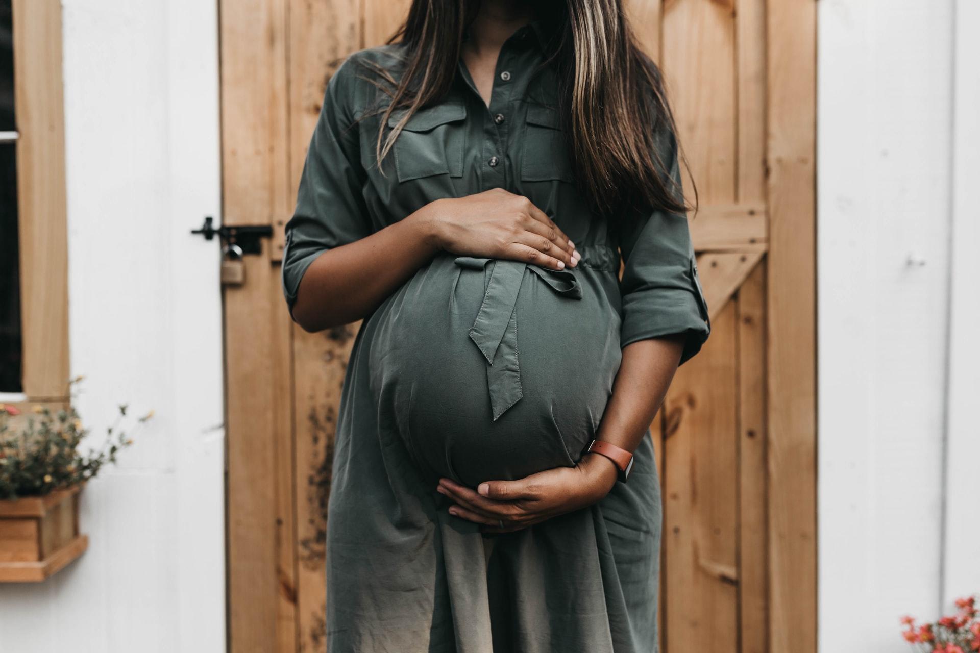 Gravid kvinna i grön klänning framför dörr