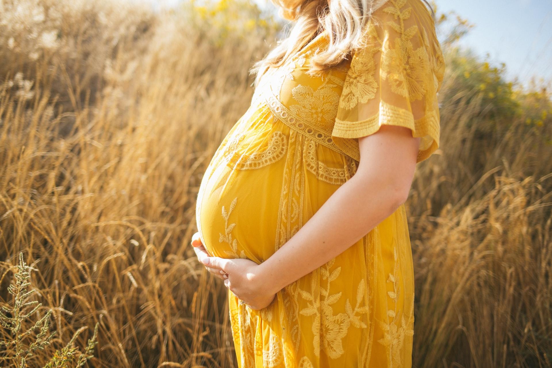 gravid kvinna i gul klänning på fält