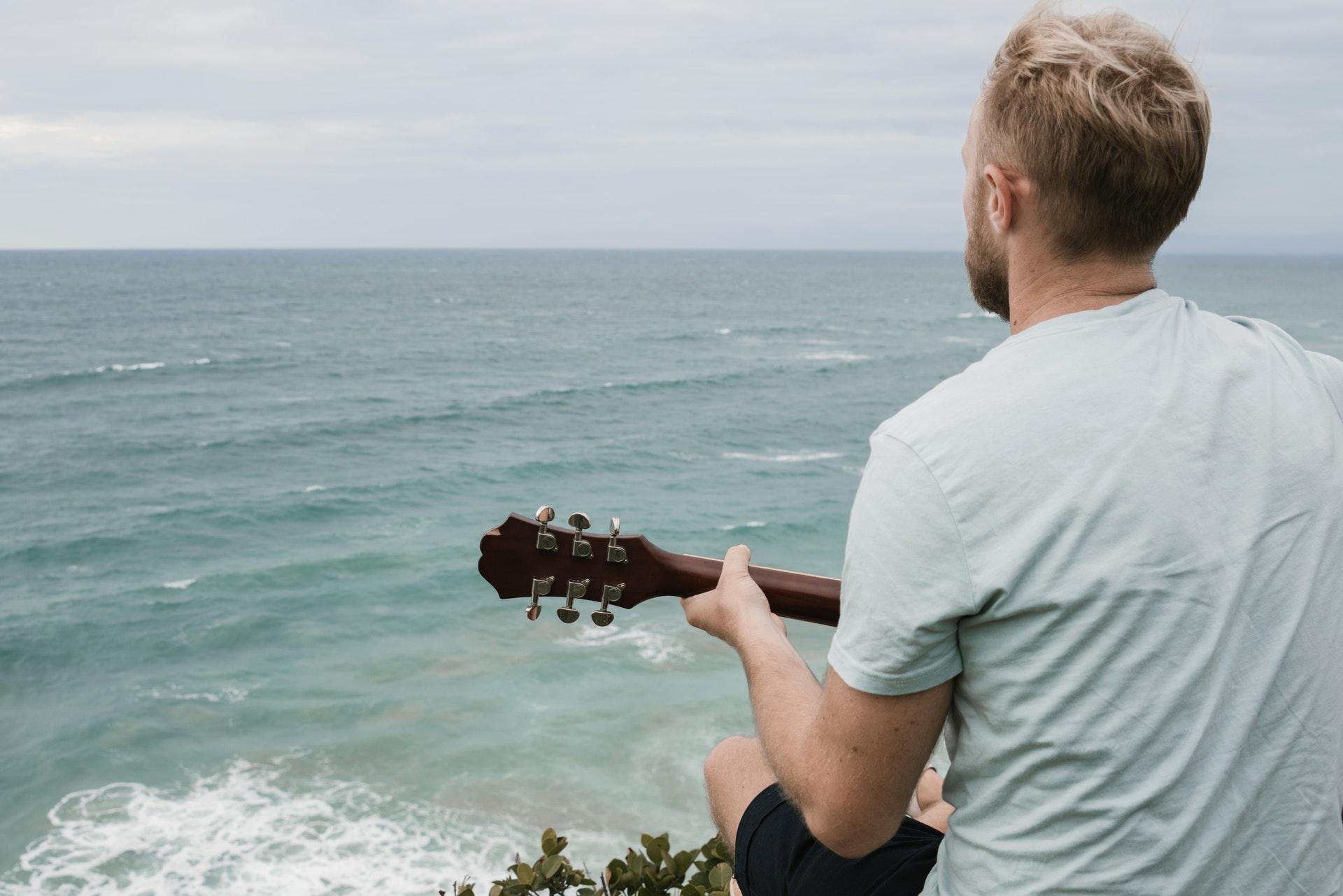 man spelar på gitarr framför havet