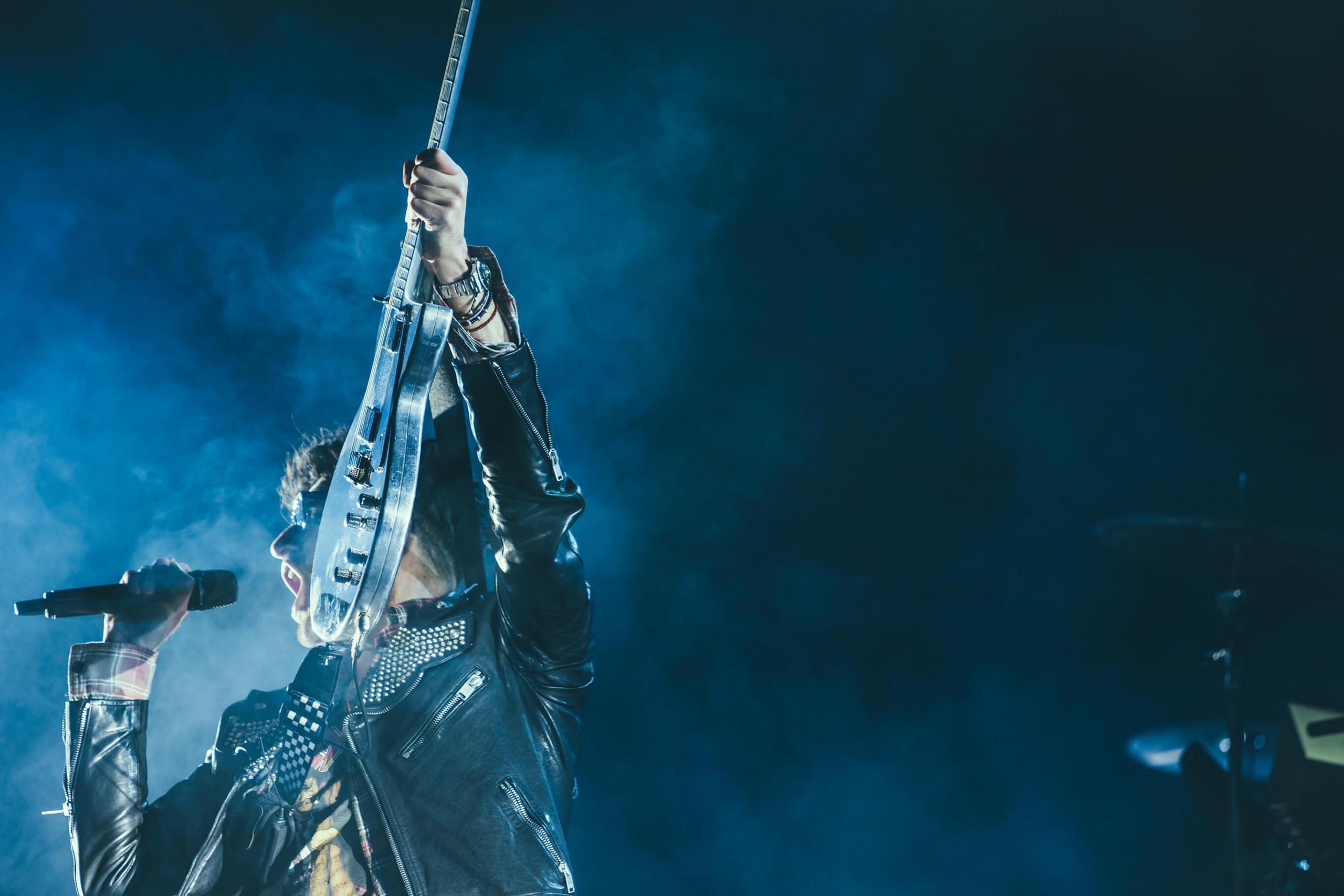 En gitarrist håller upp sin gitarr med en hand.