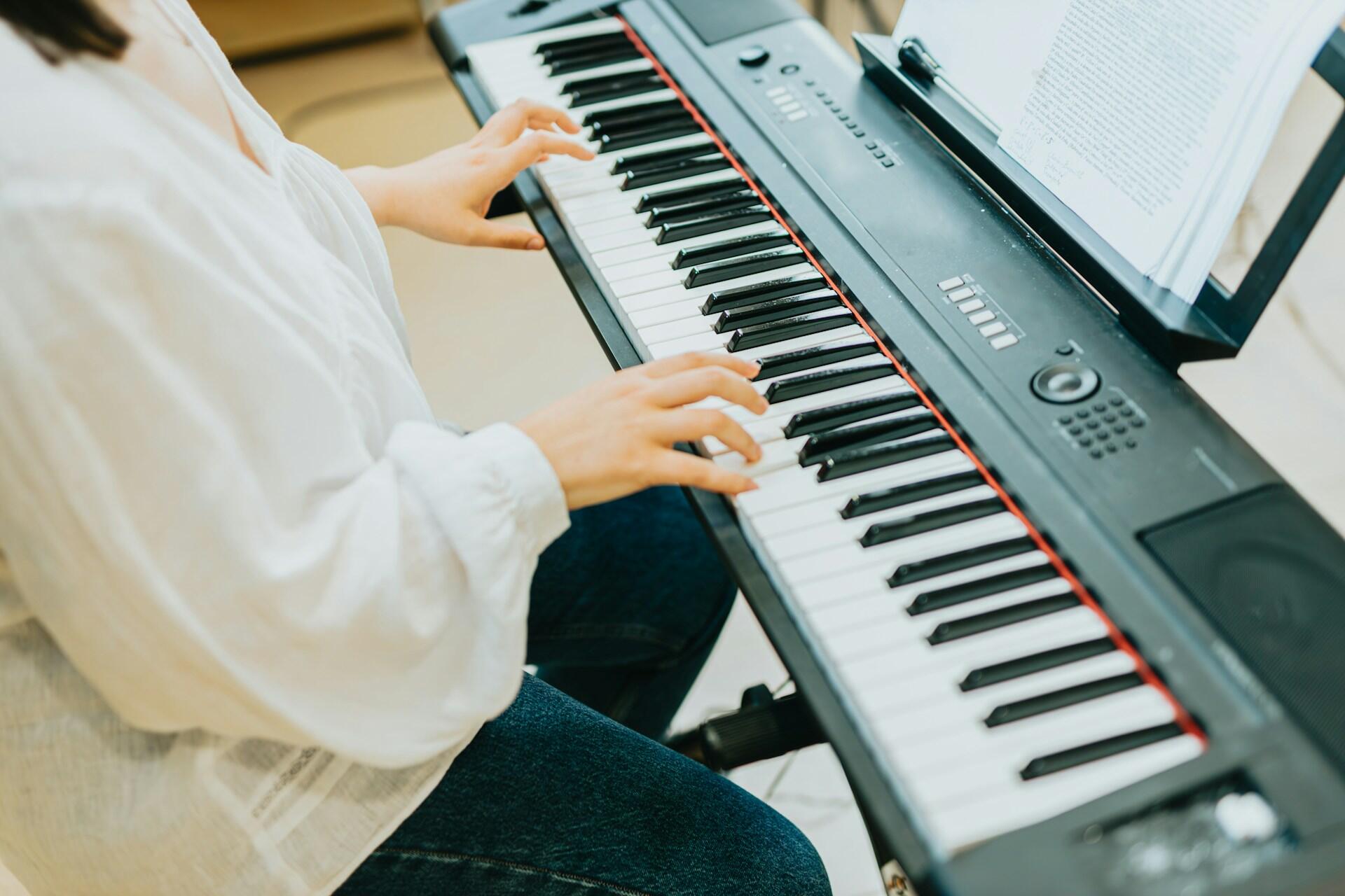 En bild tagen snett uppifrån på händer som spelar på tangenterna på ett elpiano. Bild av A. C. via Unsplash+