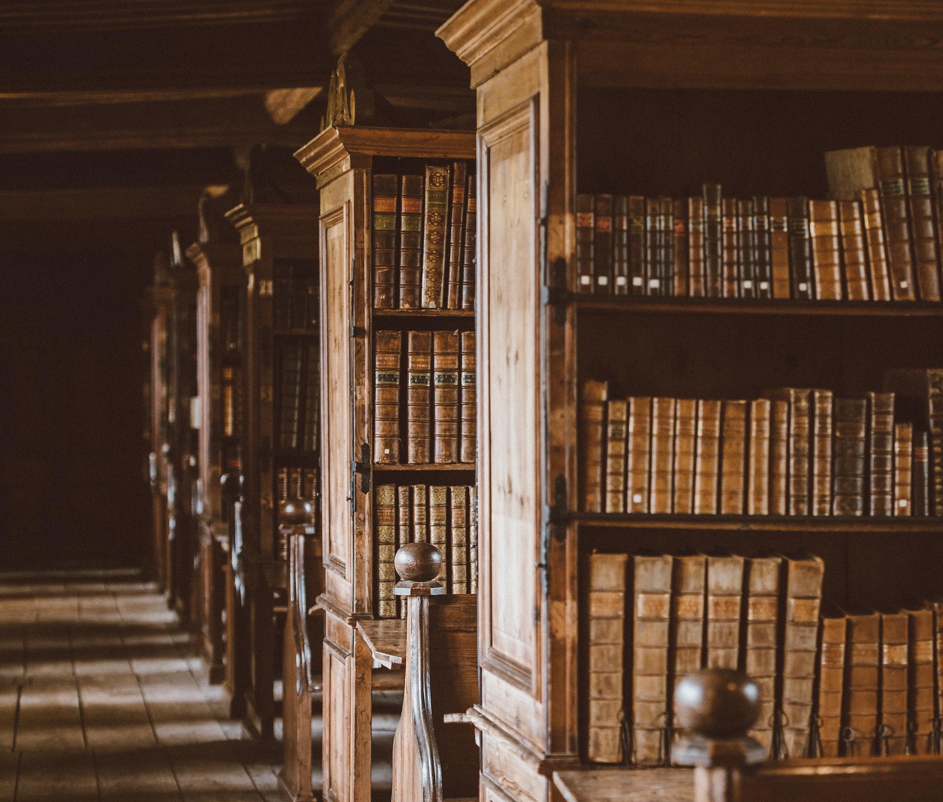 Ett bibliotek med stora, bruna bokhyllor fyllda med äldre böcker.