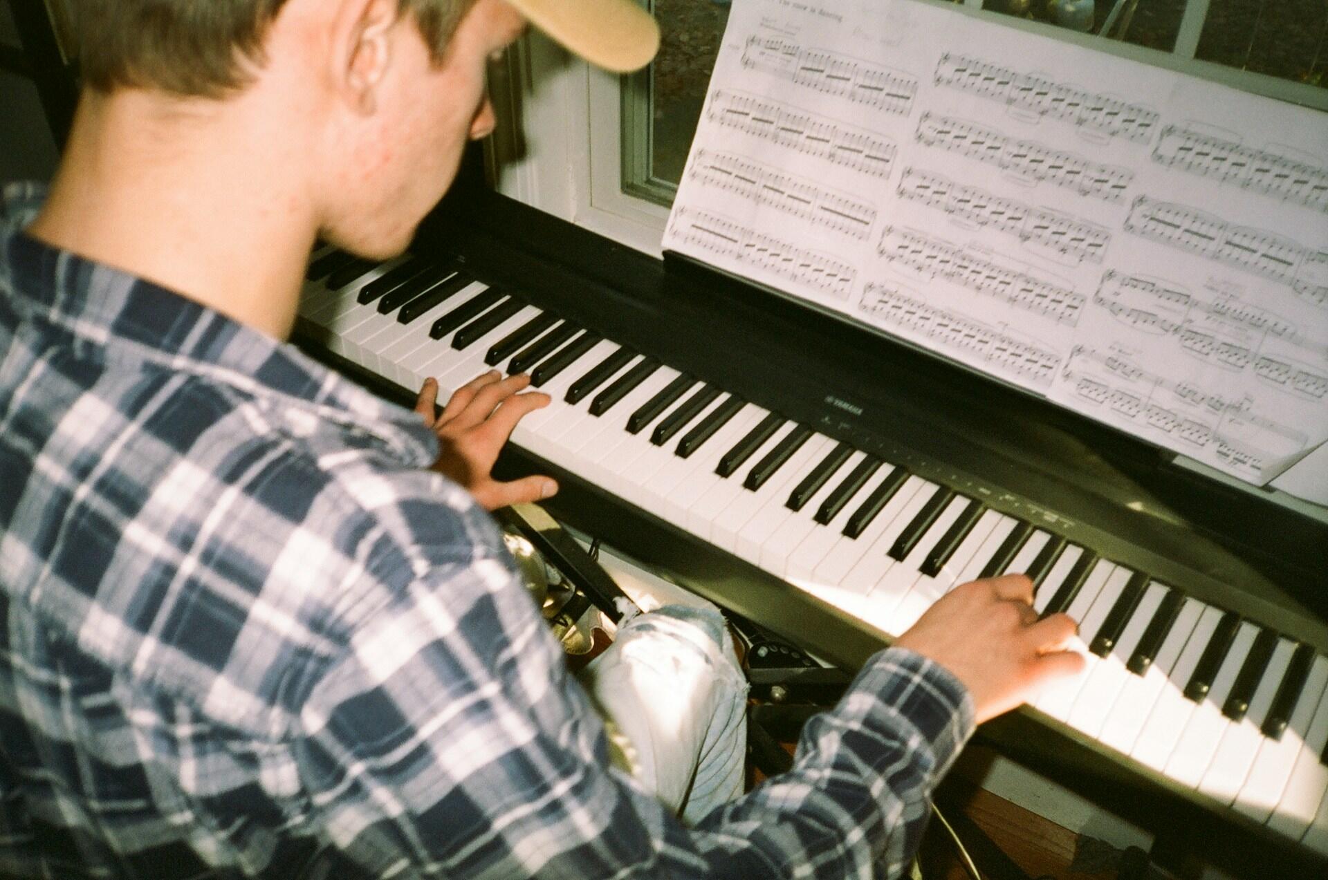 Bild tagen över axeln på en person i keps som sitter och spelar piano.