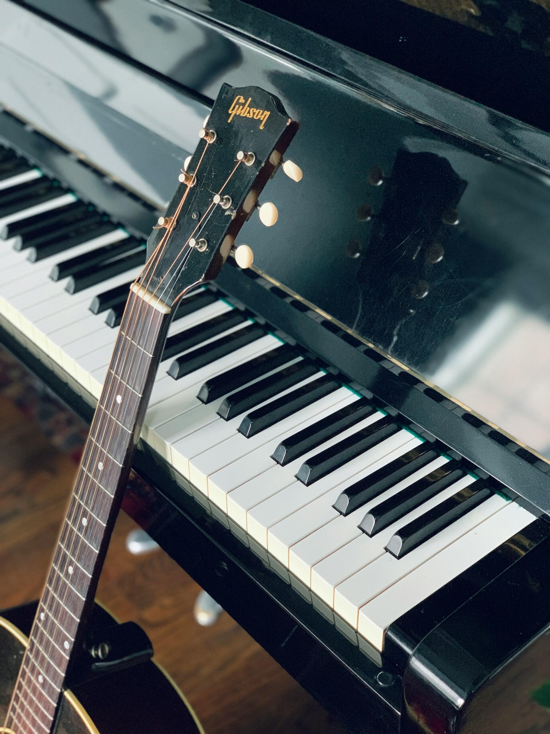 En bild på ett piano och en gitarr som står lutat mot tangenterna. Foto av Tim Wildsmith på Unsplash
