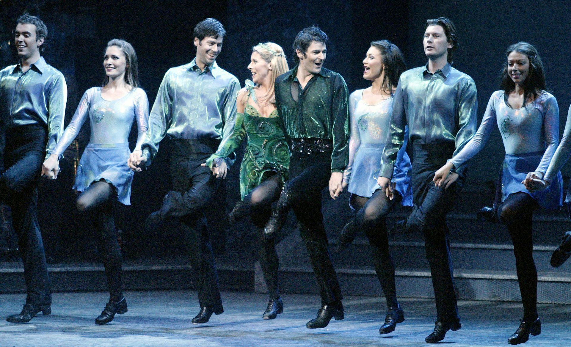 Kvinnor och män som dansa riverdance i rader uppe på en scen.
