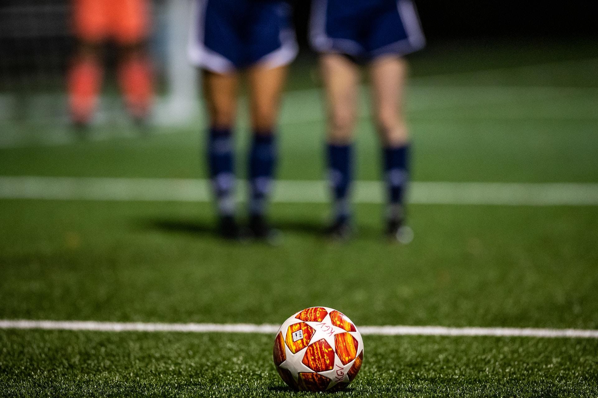 En fotboll ligger upplagd för frispark. Två spelare står framför bollen och blockerar målet.