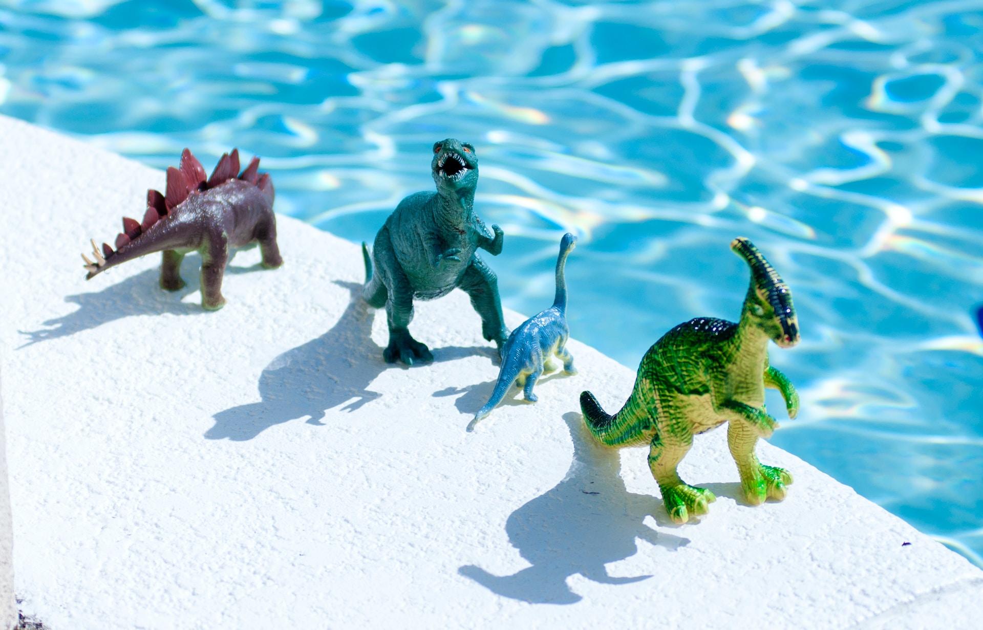 Fyra dinosaurieleksaker står uppradade längst med en poolkant.