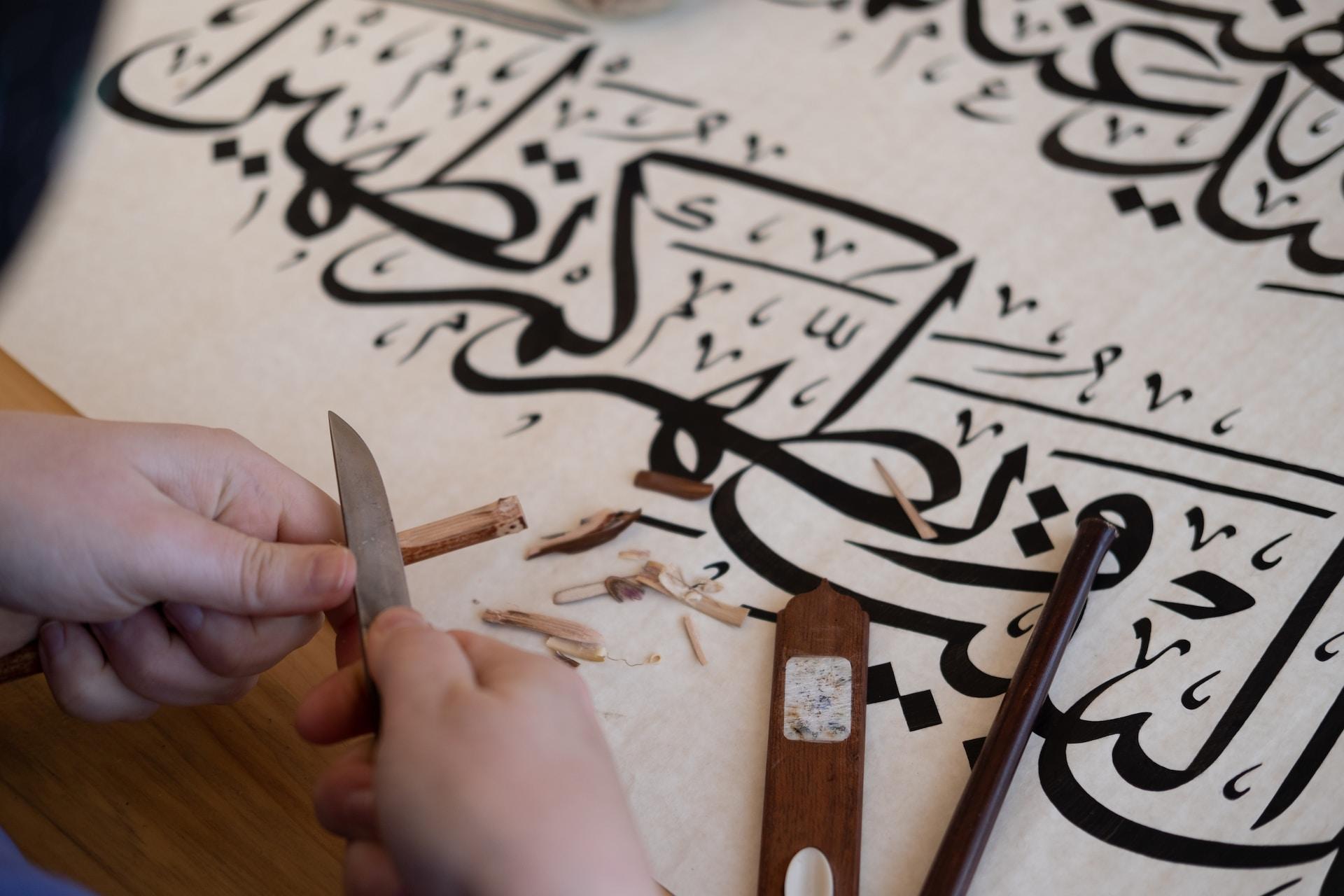 Händer som vässar en penna över ett papper med arabisk skrift.