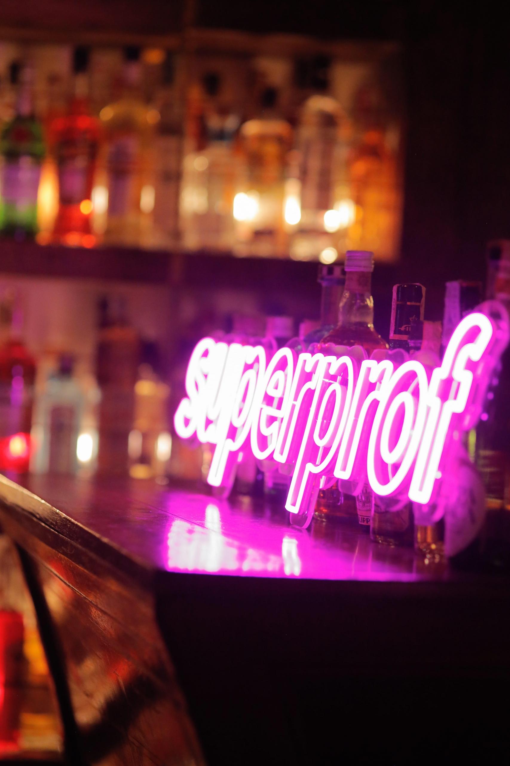 Neon-skylt med texten "superprof" uppställd på en bar.