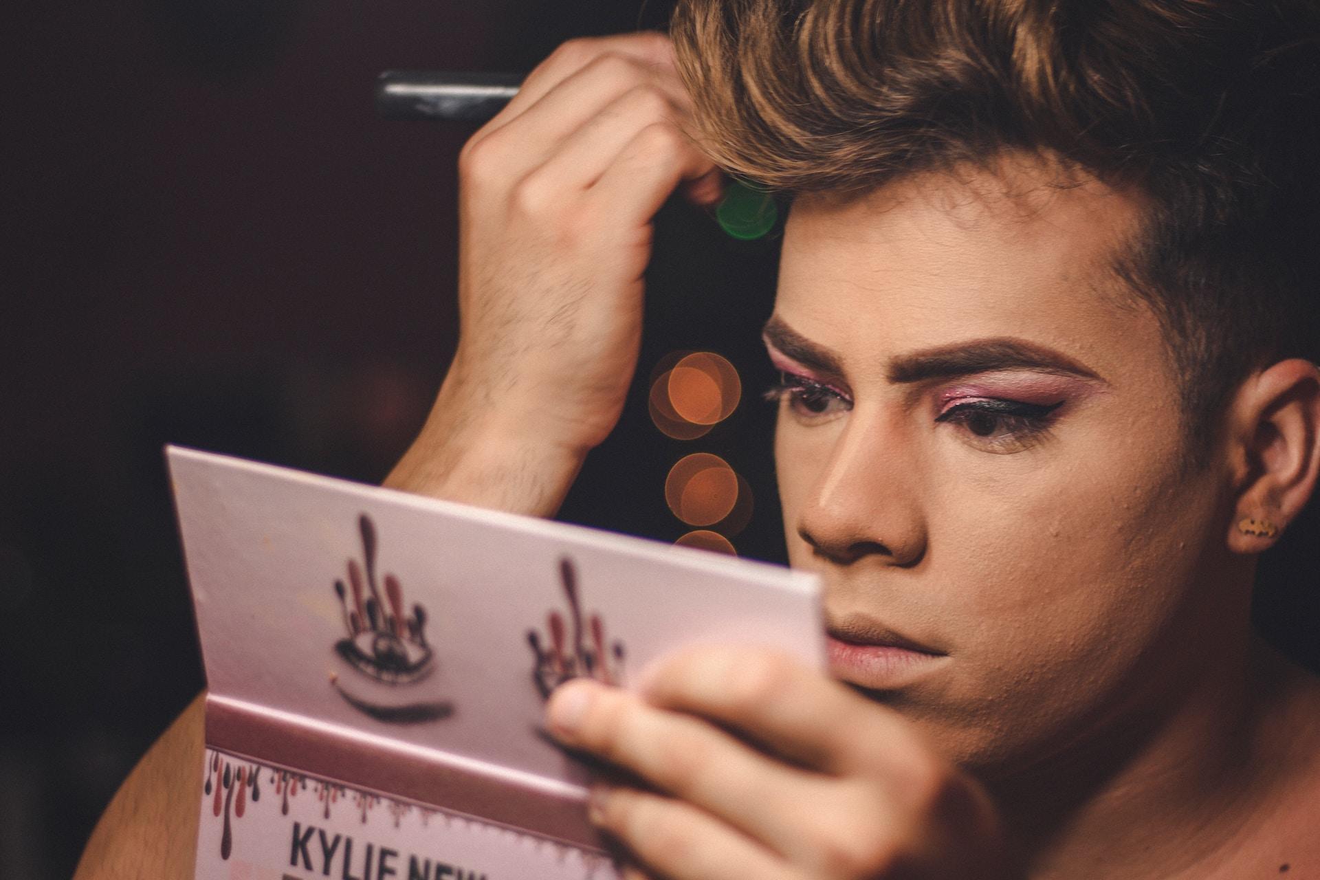 Makeup artist som sminkar sig själv med hjälp av en palett med spegel i sig.