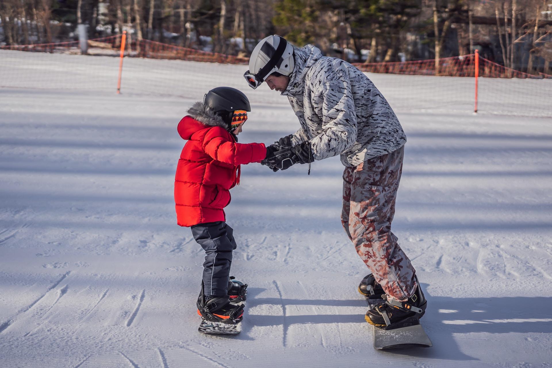 Lärare som lär ett barn åka snowboard.