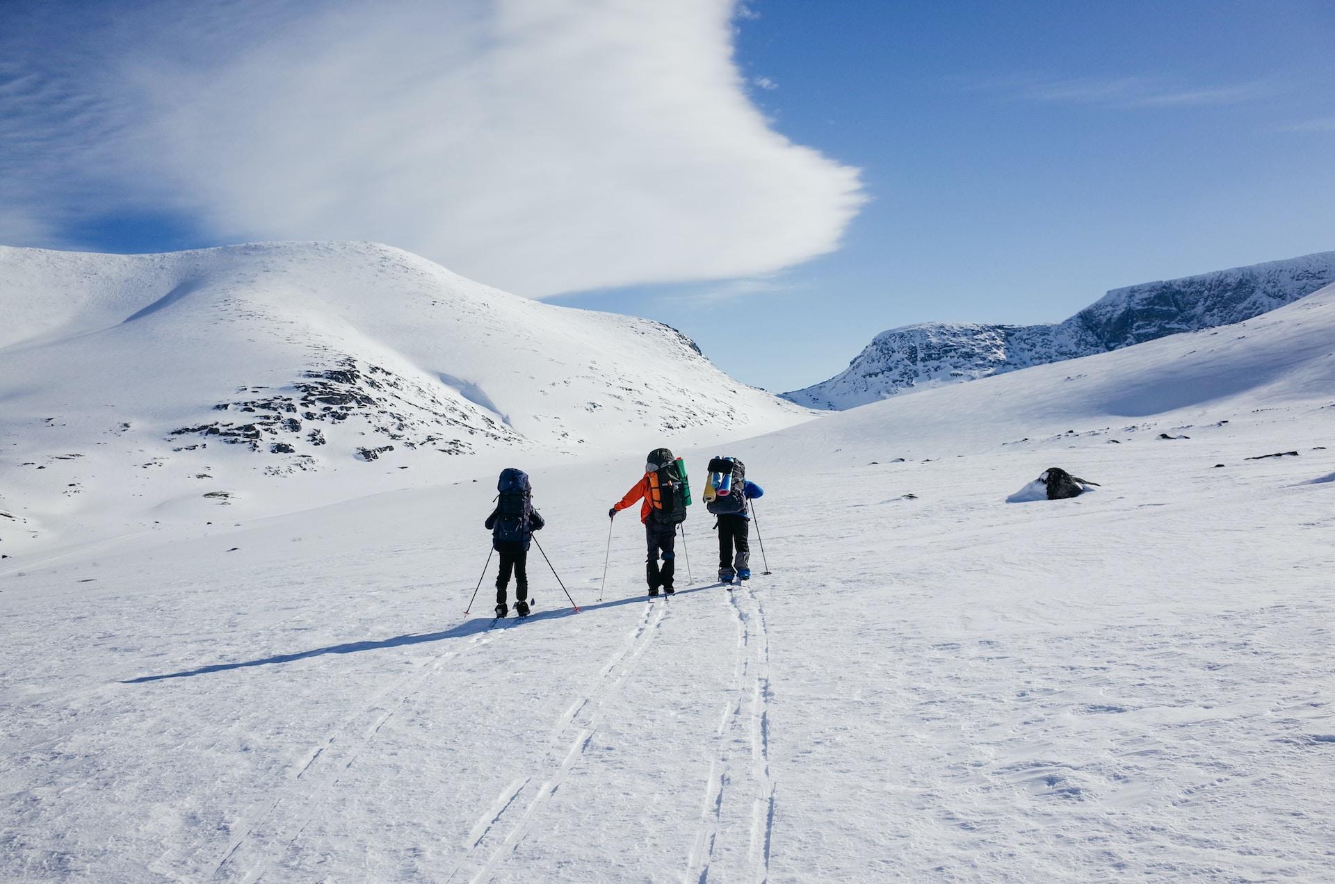 Tre skidåkare på längdskidor uppe bland bergstopparna.