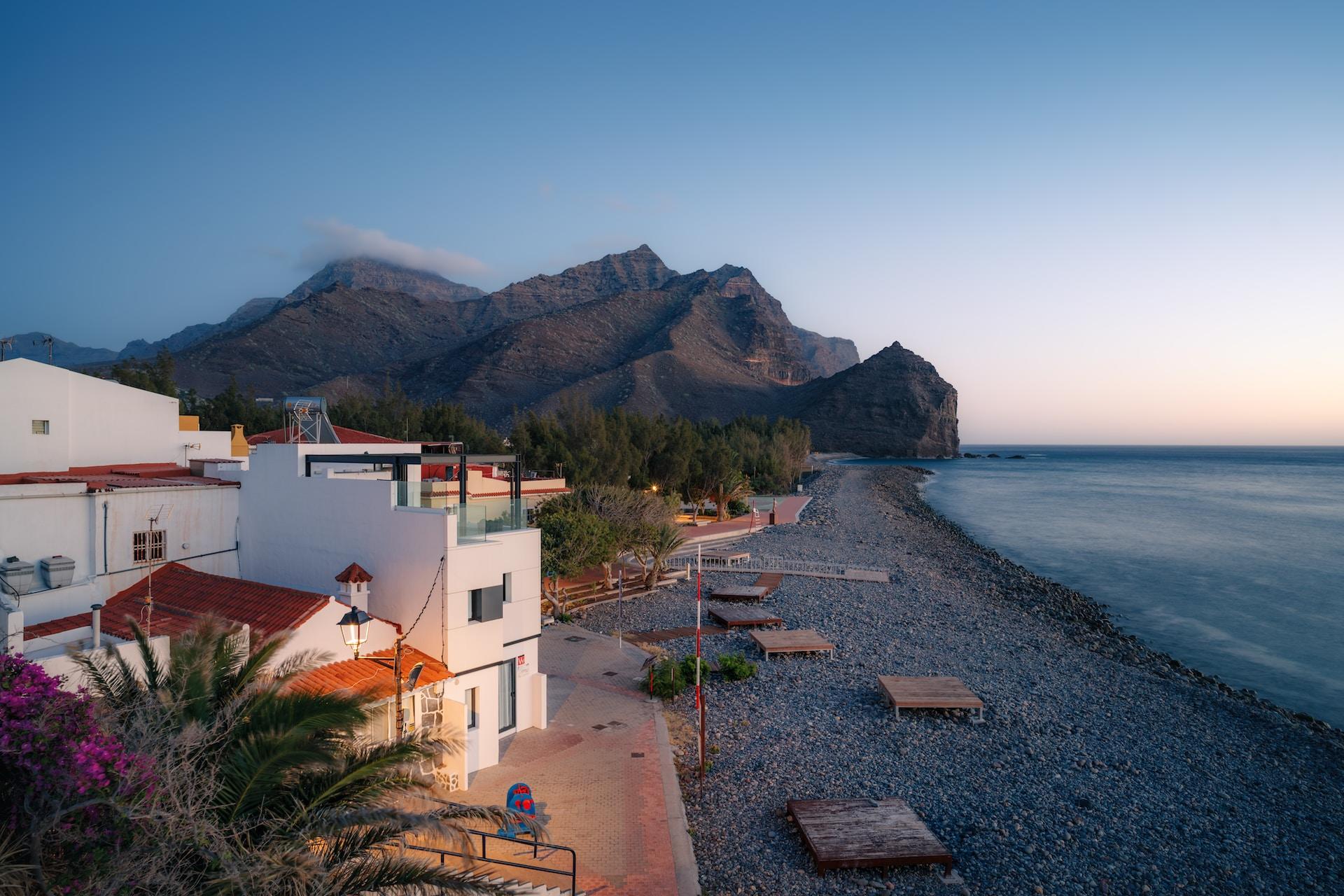 Semesterhus på stranden med berg i bakgrunden.
