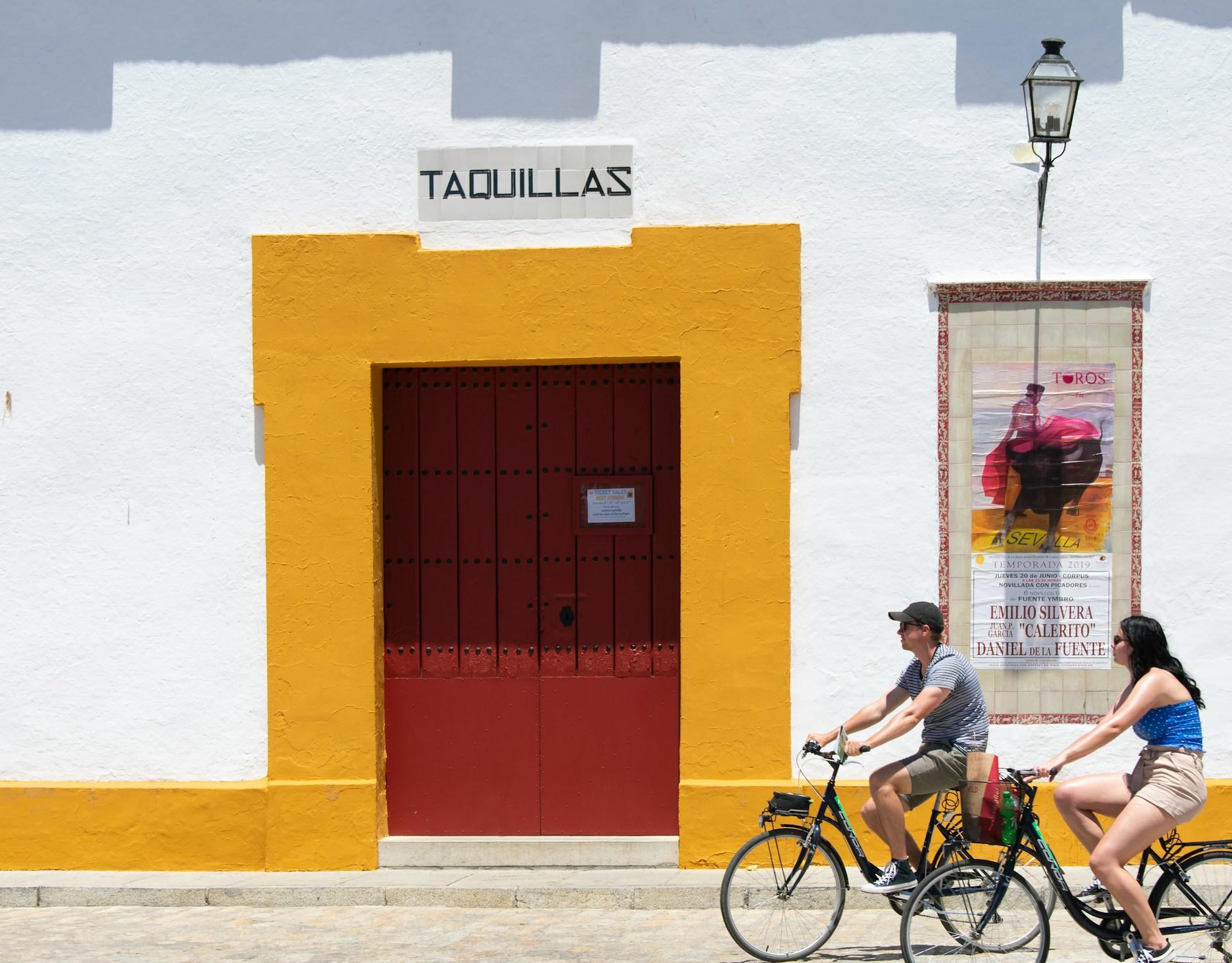 Husfasad i staden Sevilla. Två personer cyklar i bild.