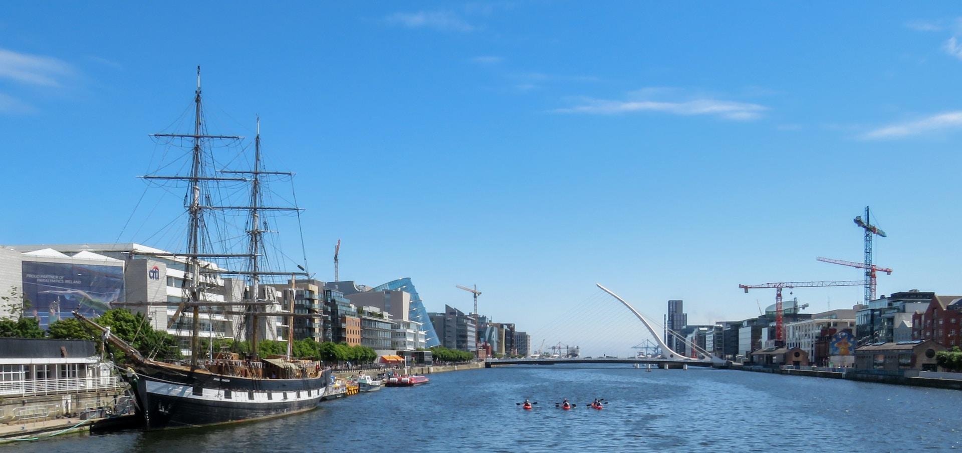 Flod i Dublin med båt, bro och trio som paddlar. 