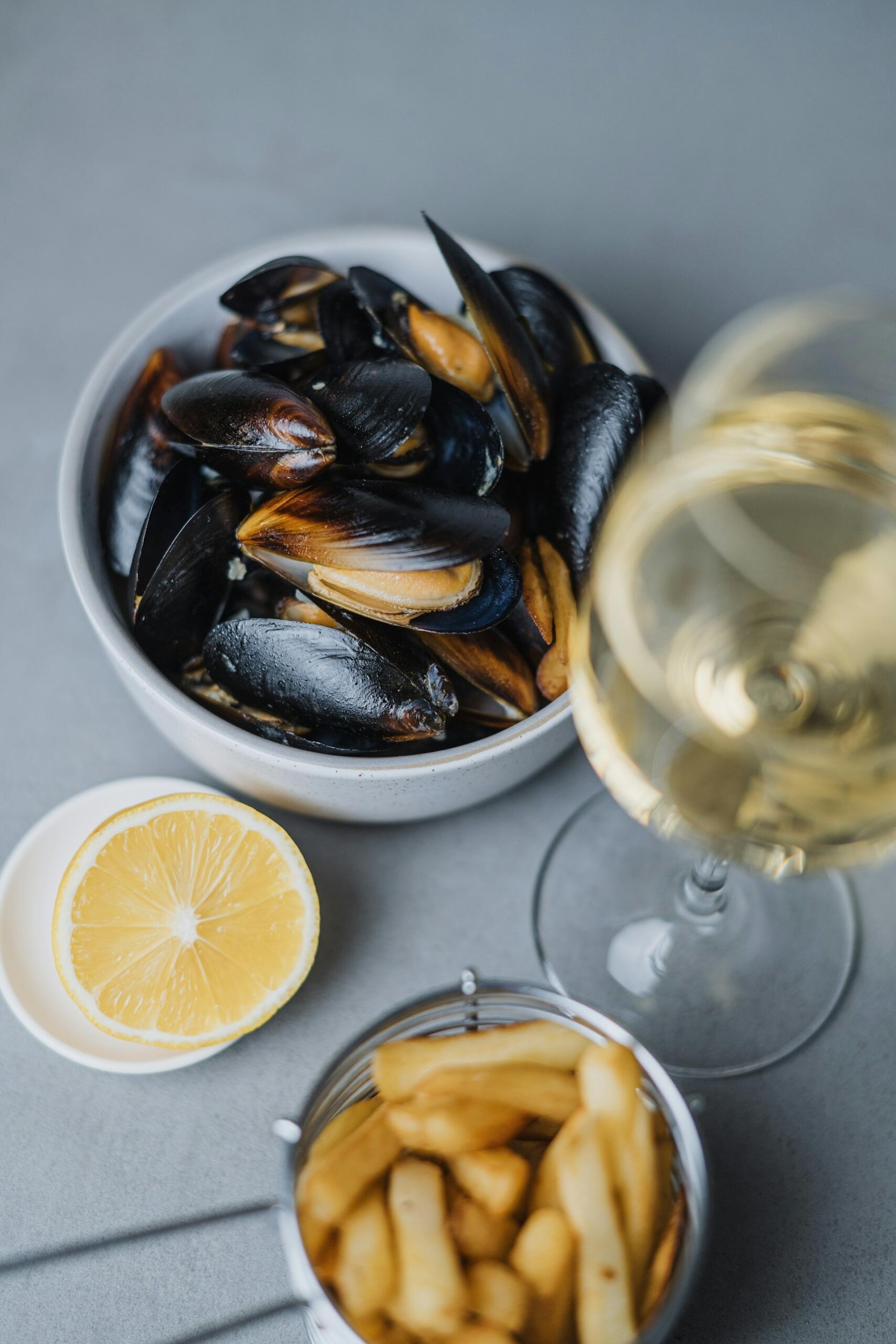 Bild på uppdukat bord med vitt vin, moules frites och en citronskiva.