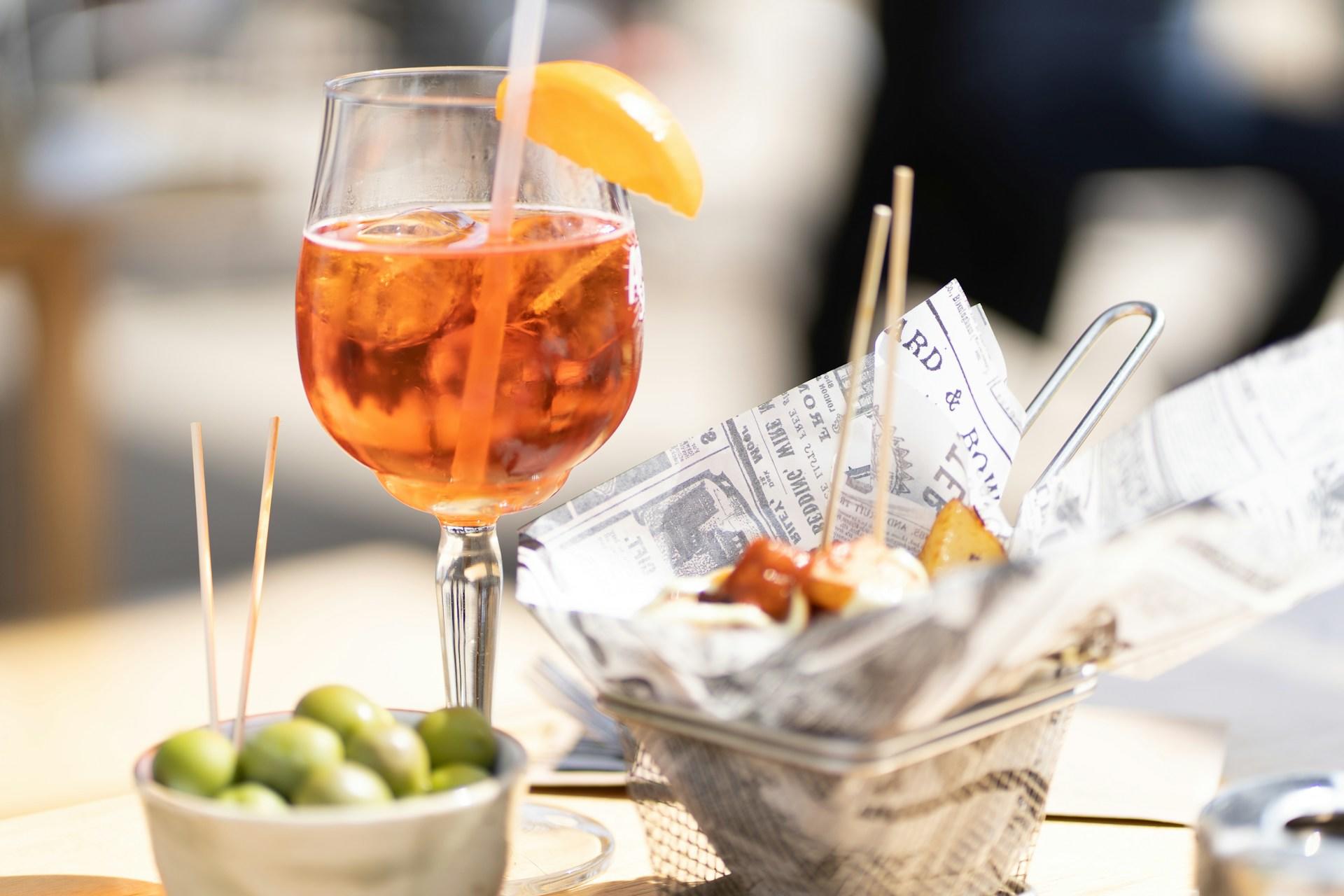 Oliver, Aperol spritz och patatas bravas på ett bord.