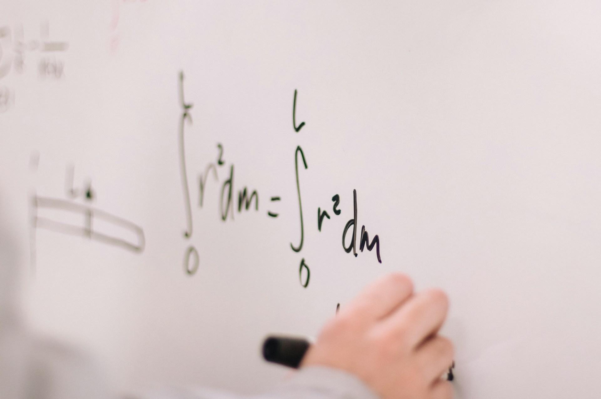 Hand som skriver matematiska formler på en witeboard.