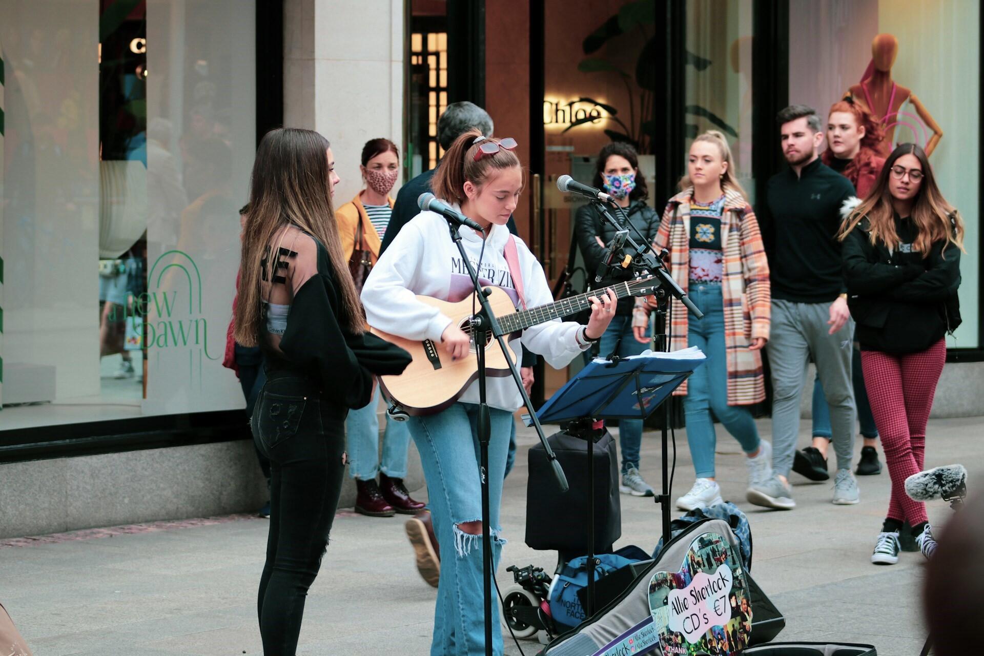 Elever som står och sjunger på gatan med gitarr och mikrofon.
