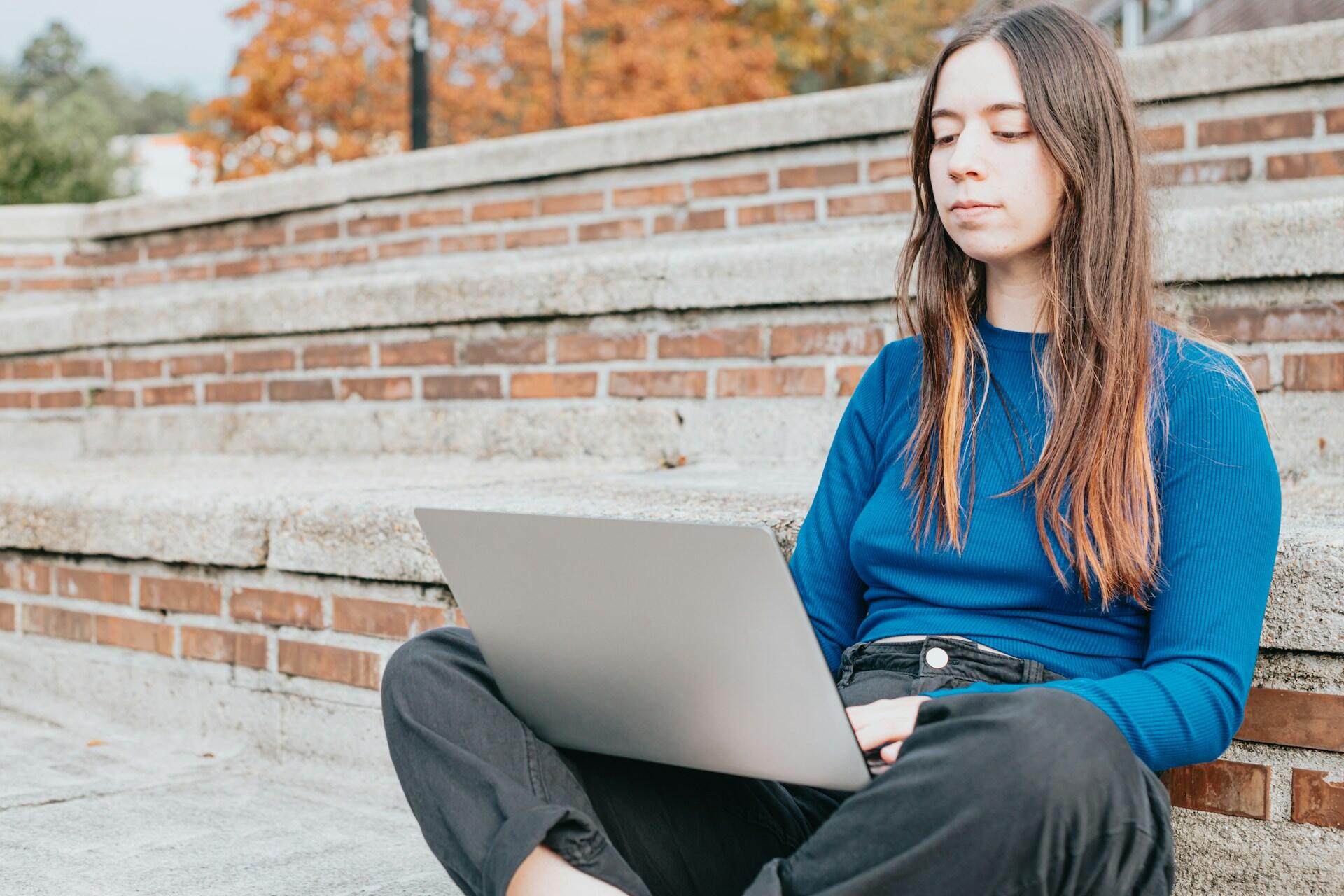 Kvinna som sitter och skriver utomhus på en laptop.