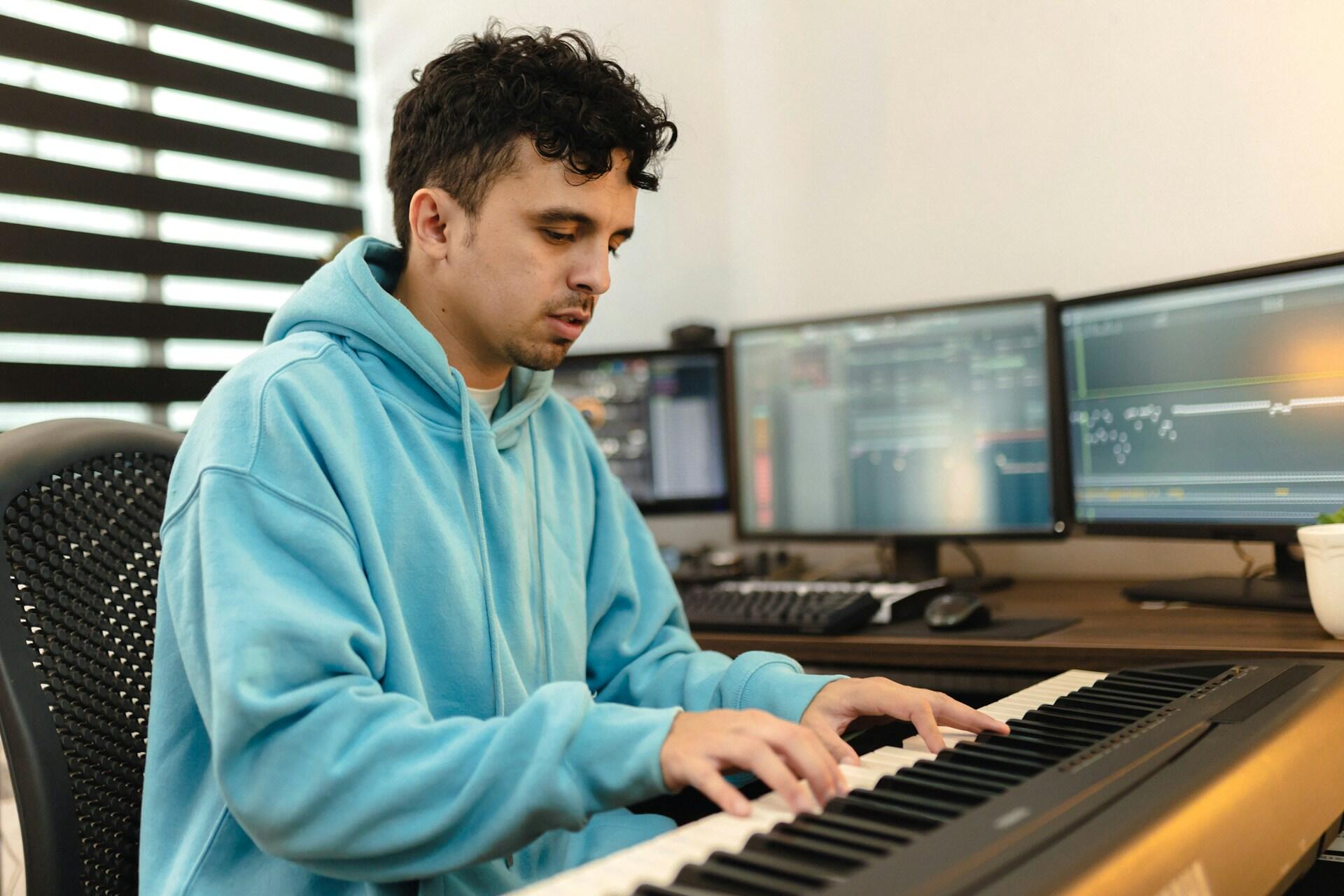 Person som sitter vid ett piano och spelar in musik på datorn.