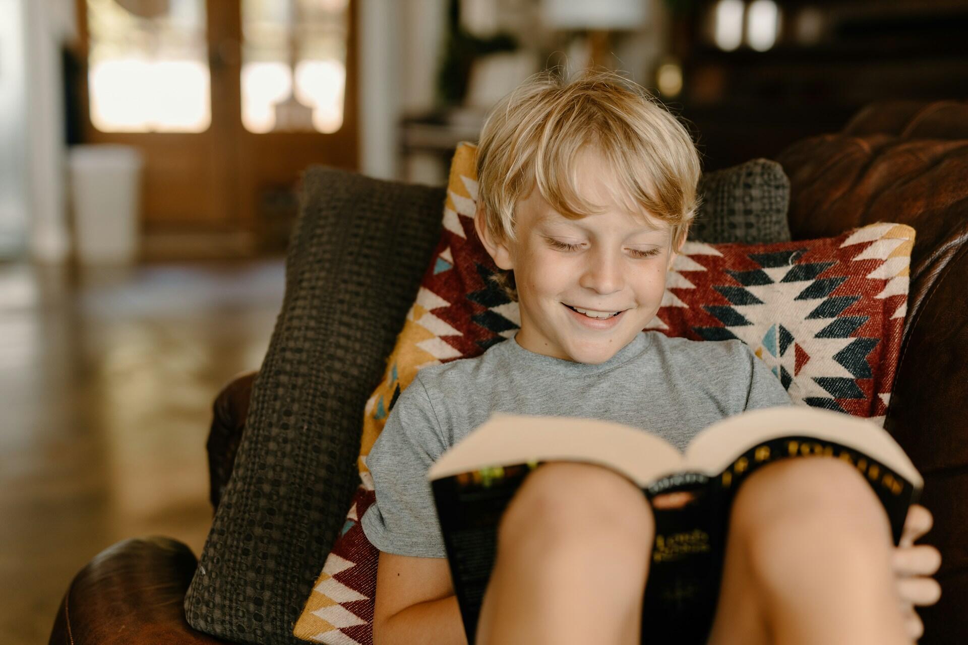 blond pojke läser bok i soffan