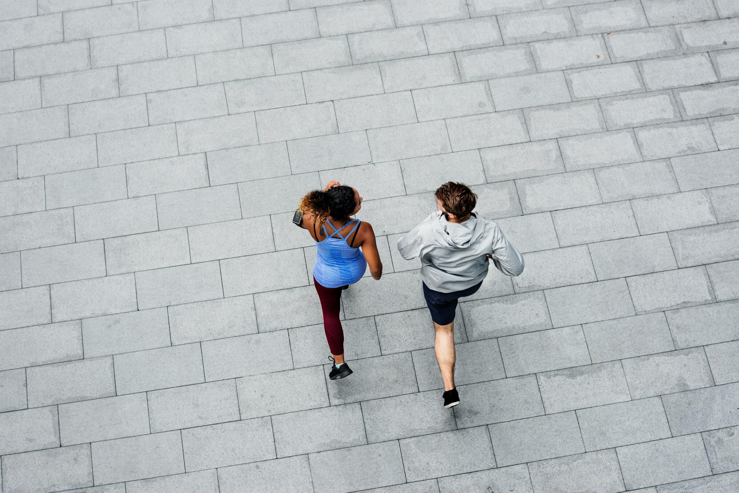en man och en kvinna joggar tillsammans över ett grått torg.