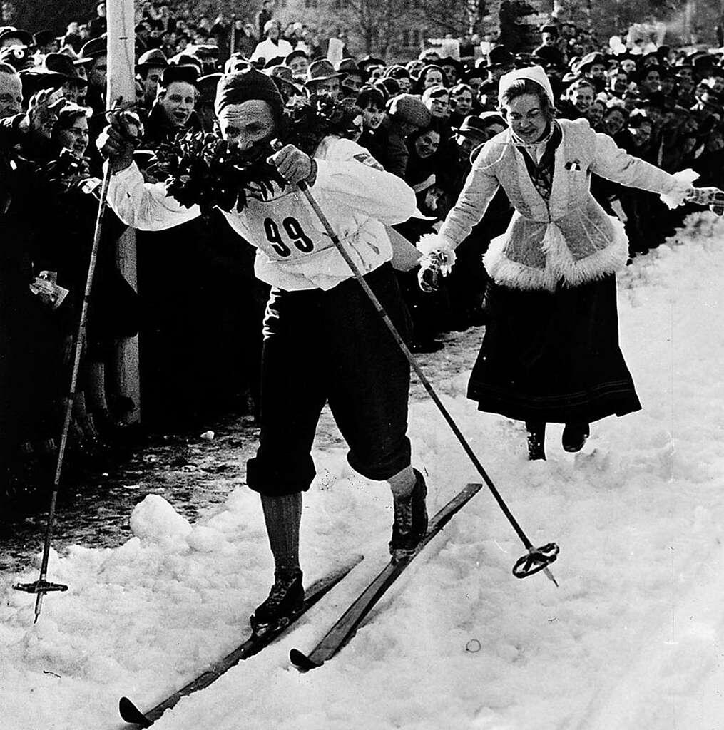  Den svenska längdskidåkaren Nils ”Mora-Nisse” Karlsson  på väg mot segern i Vasaloppet 1953. Han har just fått sin segerkrans, precis före mållinjen, av Anna-Greta Beus. Beus var ”Kranskulla” i loppet 1953.