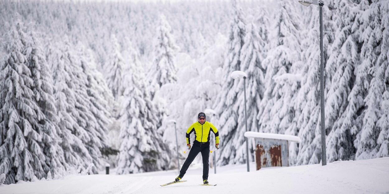 En skidåkare klädd i en knallgul jacka tar sig fram på en snötäckt stig omgiven av täta, snötäckta träd.