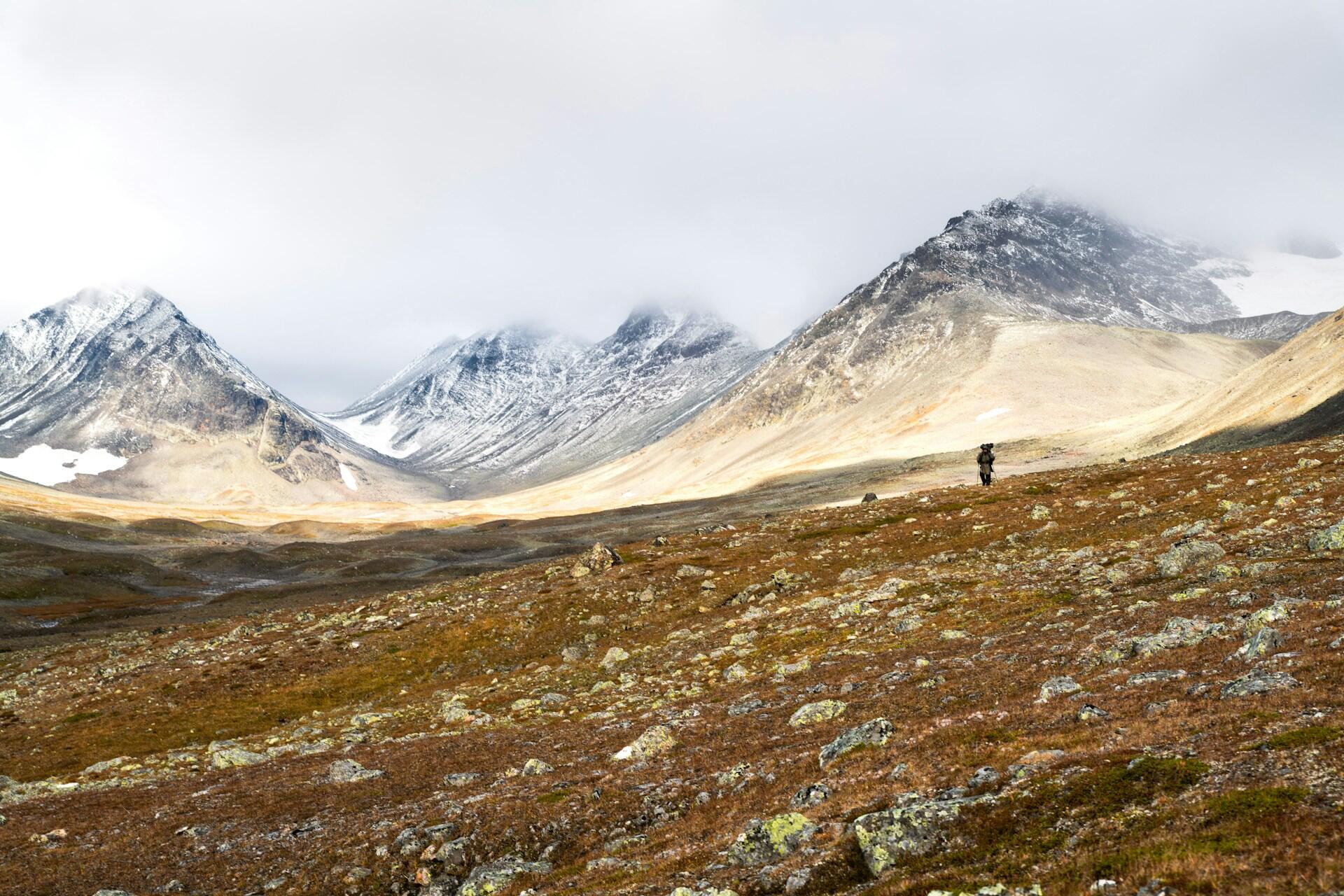 En man som går över grönt område med böljande berg i bakgrunden.
