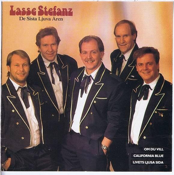 En grupp på fem män i formella svarta kostymer med kontrasterande kantband poserade tillsammans mot en mjuk, ljus bakgrund.