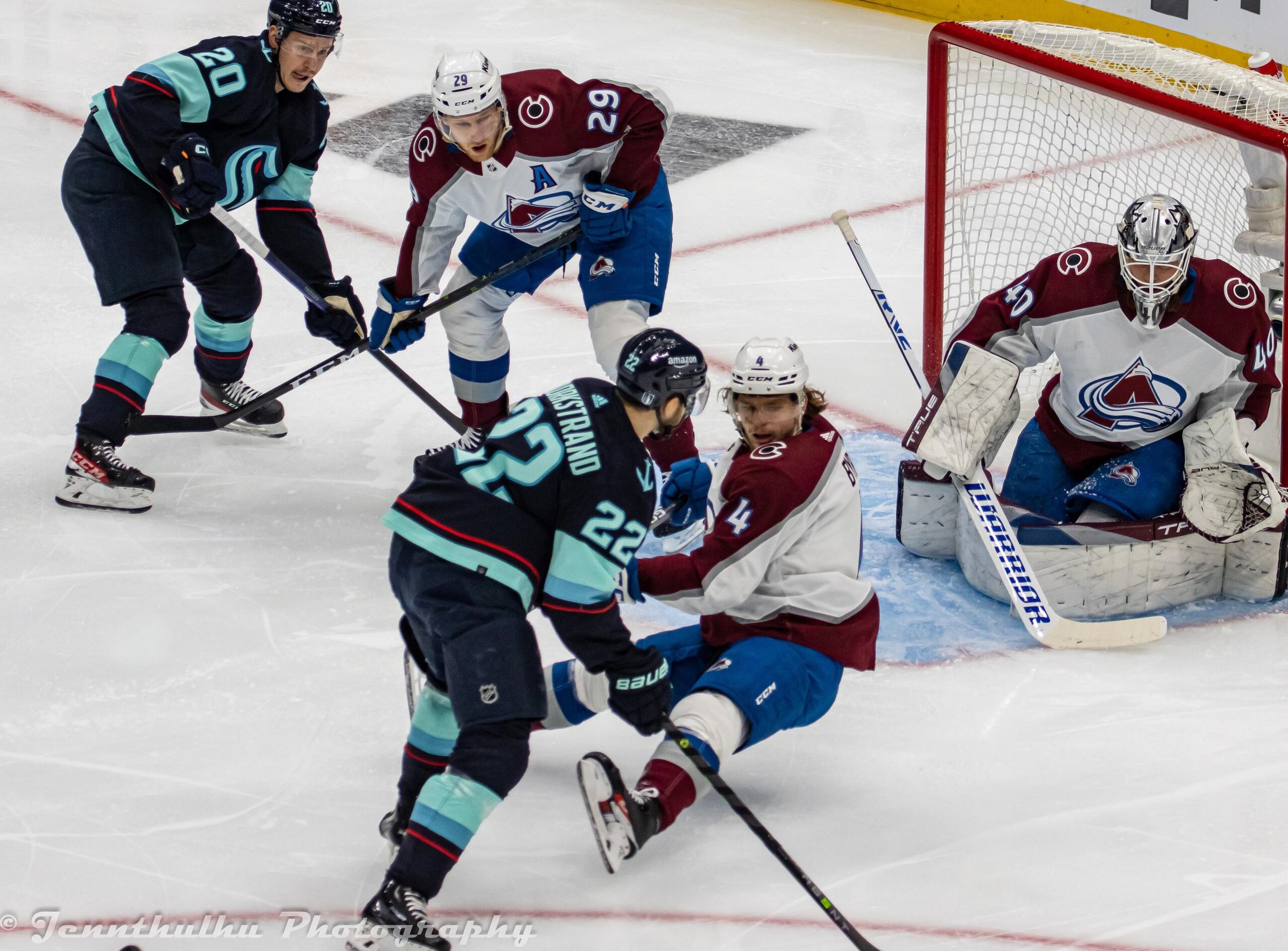 En spännande ishockeymatch med spelare i full fart, med fokus på en spelare från det svarta laget som kämpar mot motståndarna i den blå zonen.