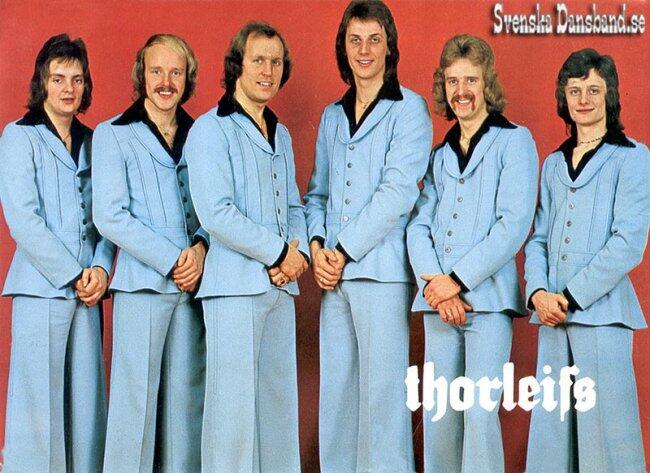 En grupp på sex män klädda i matchande ljusblå kostymer står tillsammans mot en röd bakgrund, med texten ”Thorleifs” i vitt längst ner.