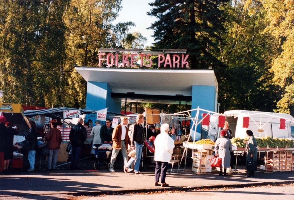 En livlig utomhusmarknad i Folkets Park, med olika stånd och besökare som strosar omkring bland färgglada höstlöv.