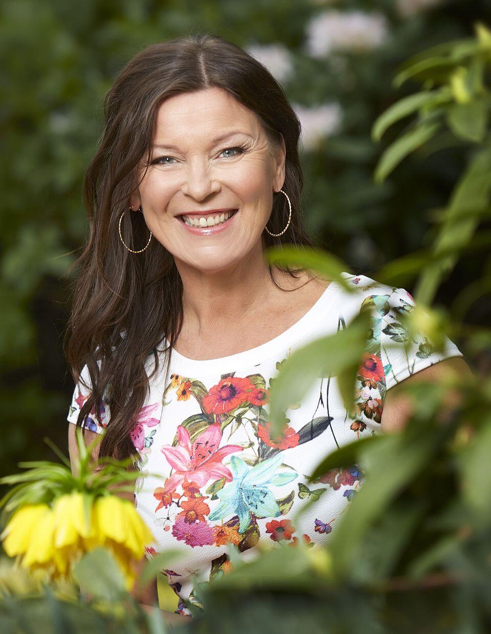 Lotta Engberg omringad av gröna blad och blommor. Porträtt som togs inför hennes sommarprat i P1.