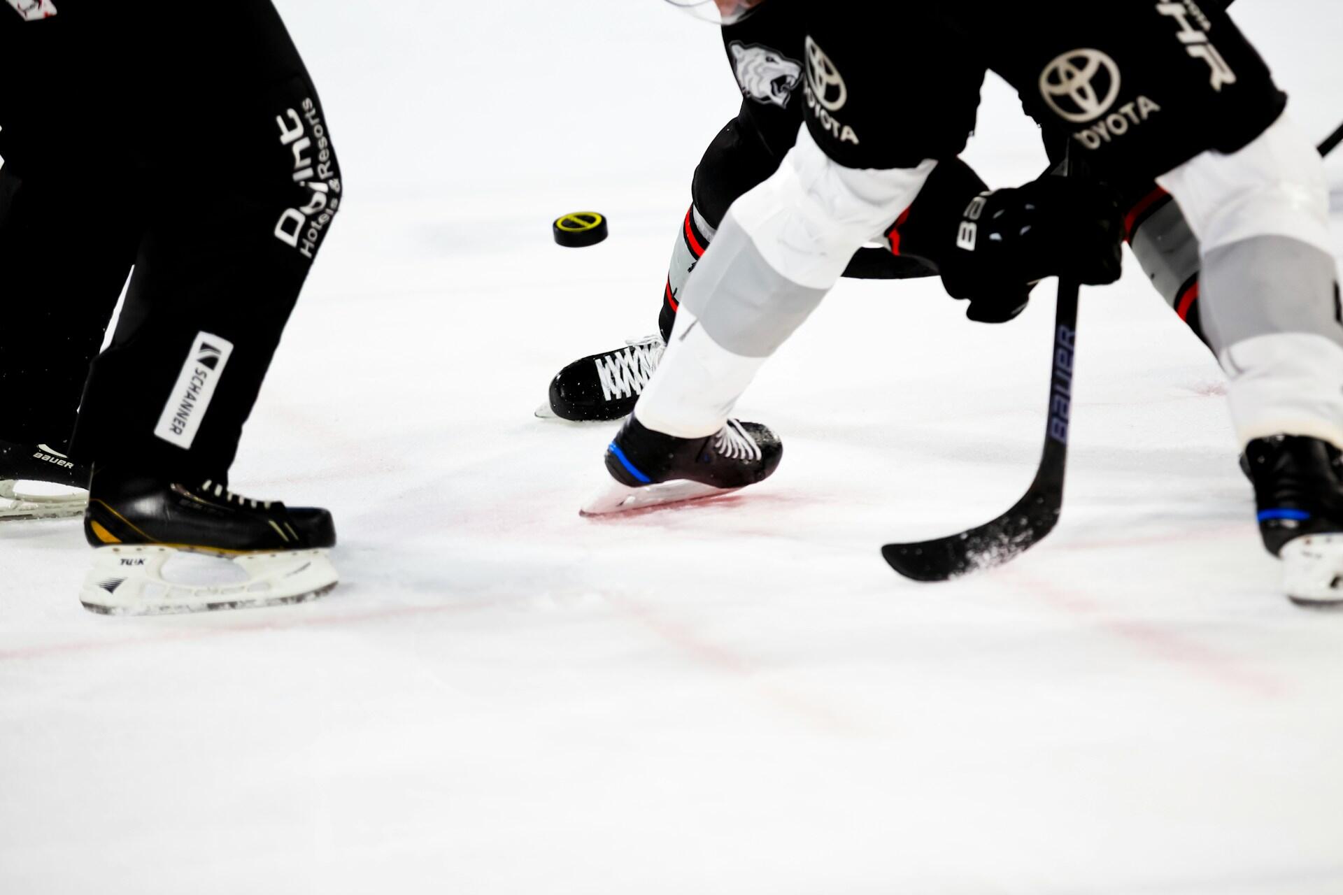 Två ishockeyspelare i svarta och vita uniformer kämpar om en puck på isen, med skridskor som glider över isytan.
