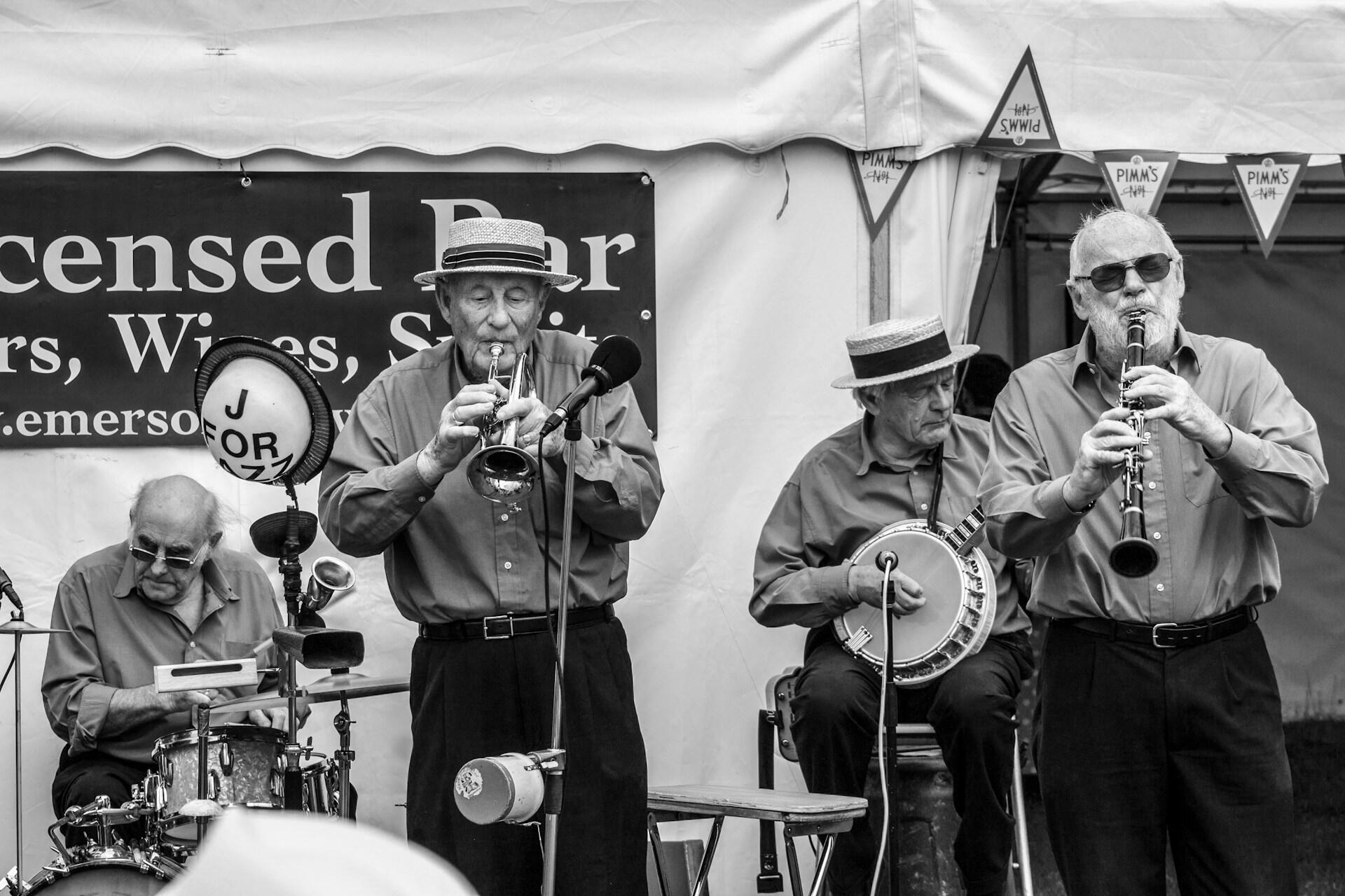 Svartvit bild på fyra äldre män som spelar olika instrument på en scen framför ett tält. I bilden syns bland annat en banjo.