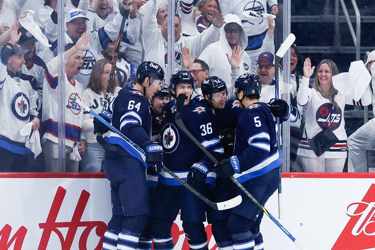 Spelare i NHL-laget Winnipeg Jets ståt i liten grupp nedanför sargen på isen. Bakom dem syns fans iklädda deras förger.