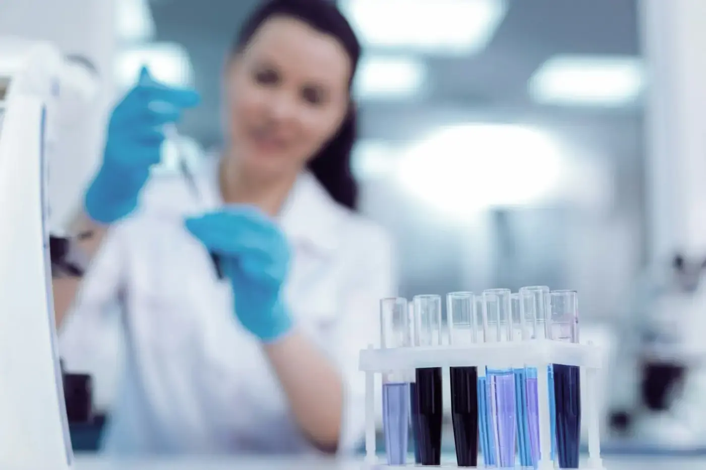 Kvinnlig forskare analyserar prover i laboratorium med provrör och skyddshandskar