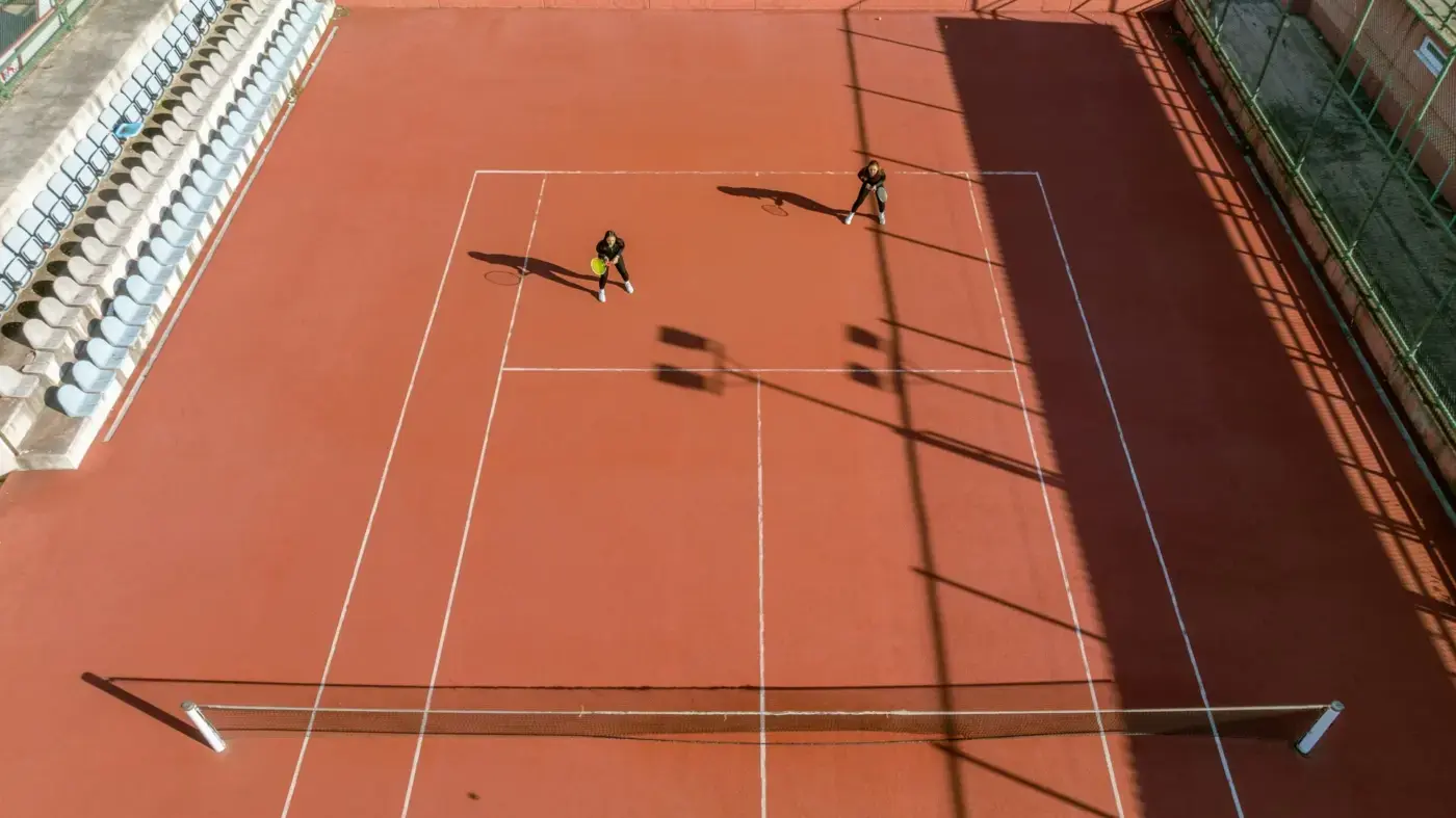 Två spelare på en tennisbana på samma sida nätet. Endast halva planen syns med de kör en dubbelmatch.