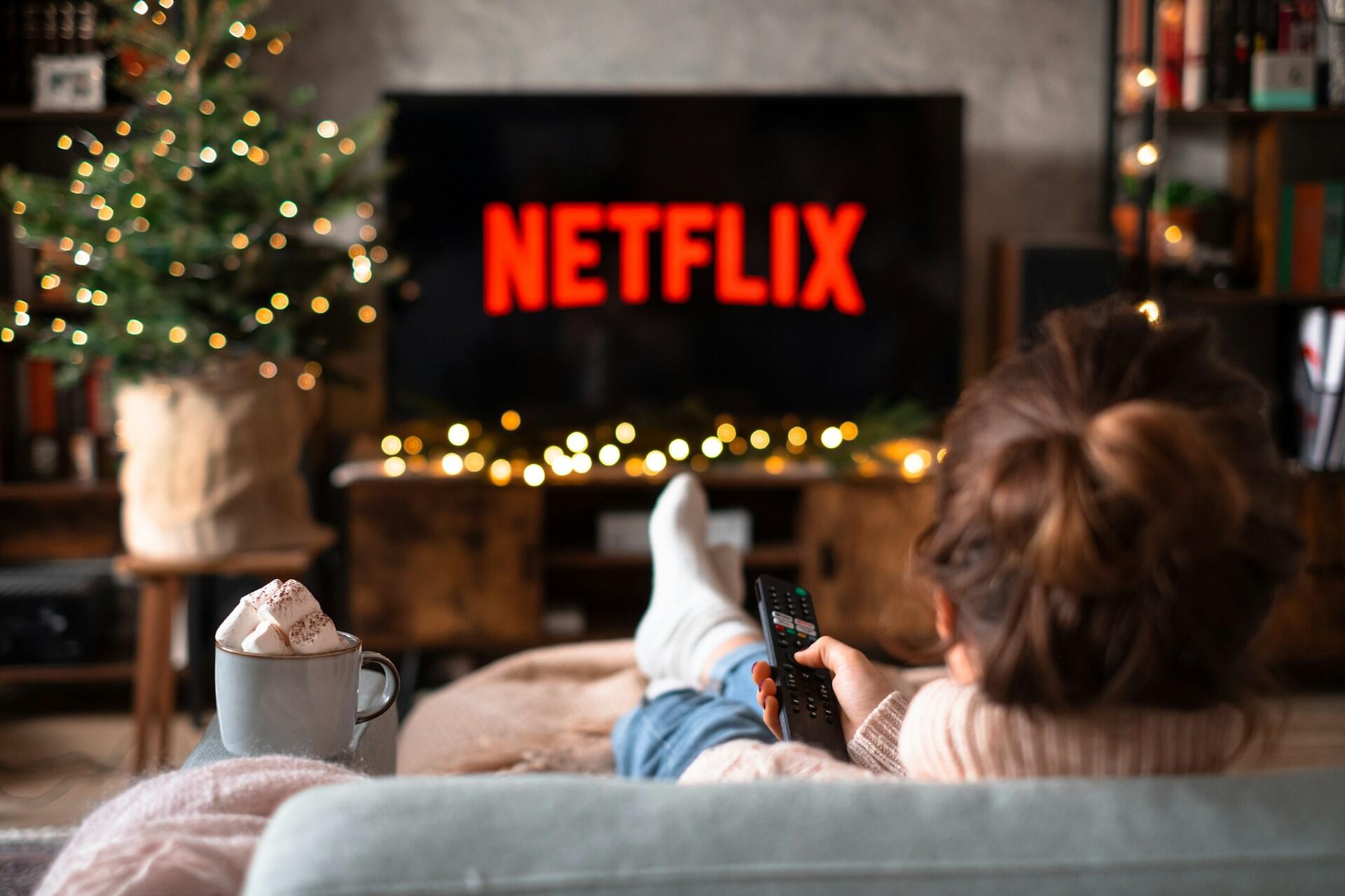 Person i soffa tittar på julfilm på Netflix i ett julpyntat vardagsrum.