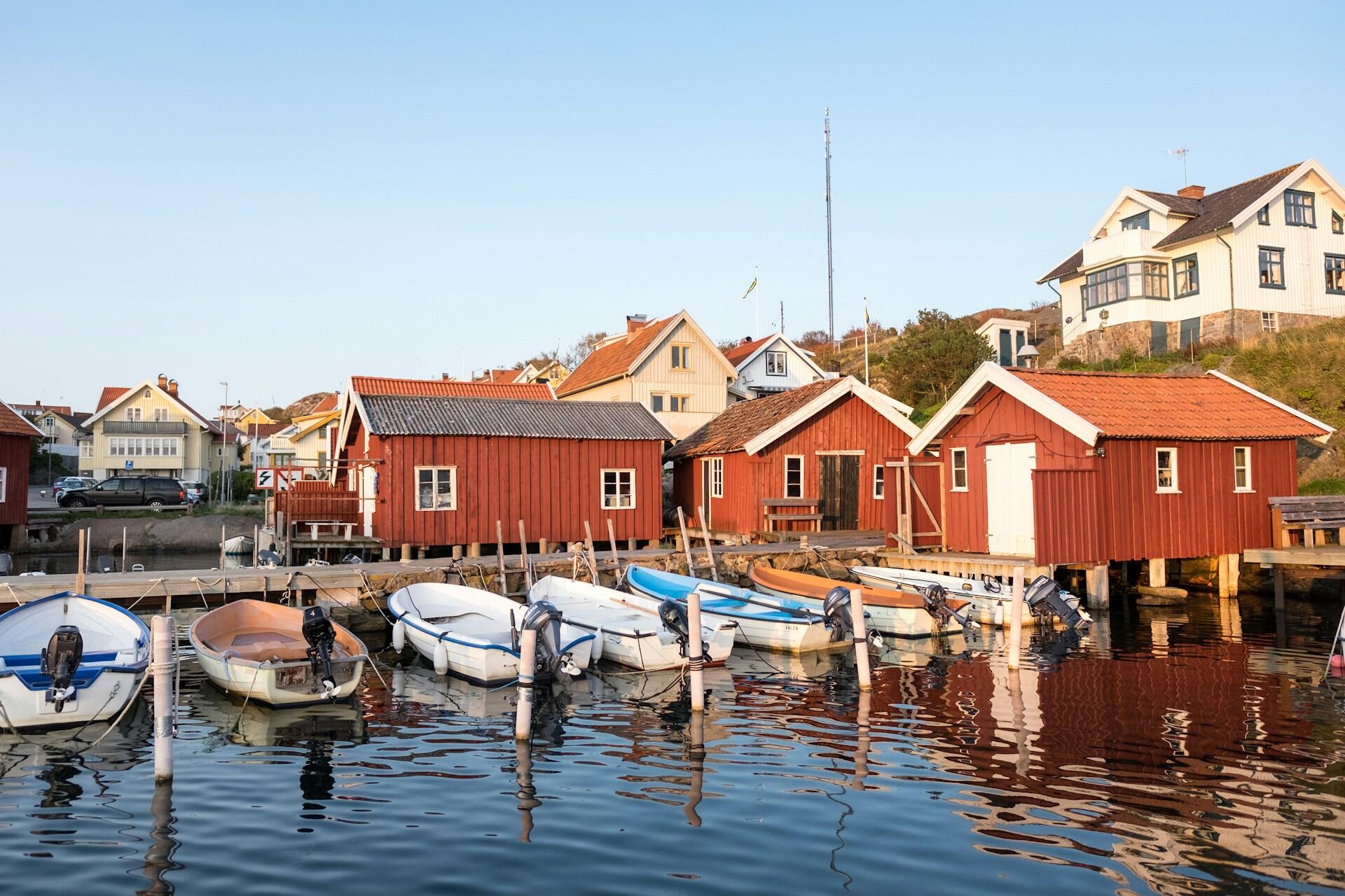Båtar förtöjda vid en brygga i havet. Bakom ser man hus och gröna buskar.